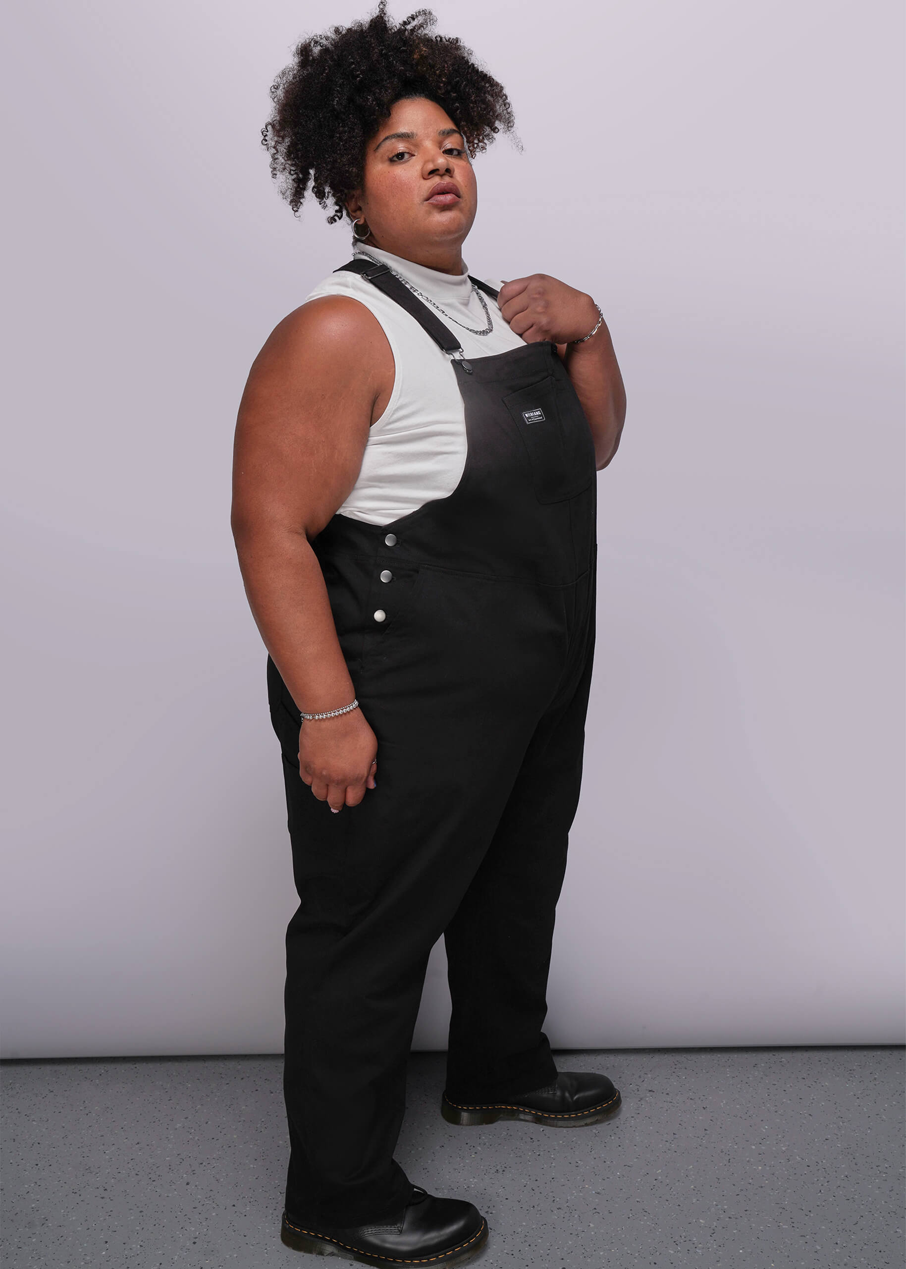 1X=Person wearing black overalls over a white shirt against a plain background