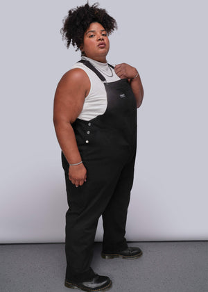1X=Person wearing black overalls over a white shirt against a plain background