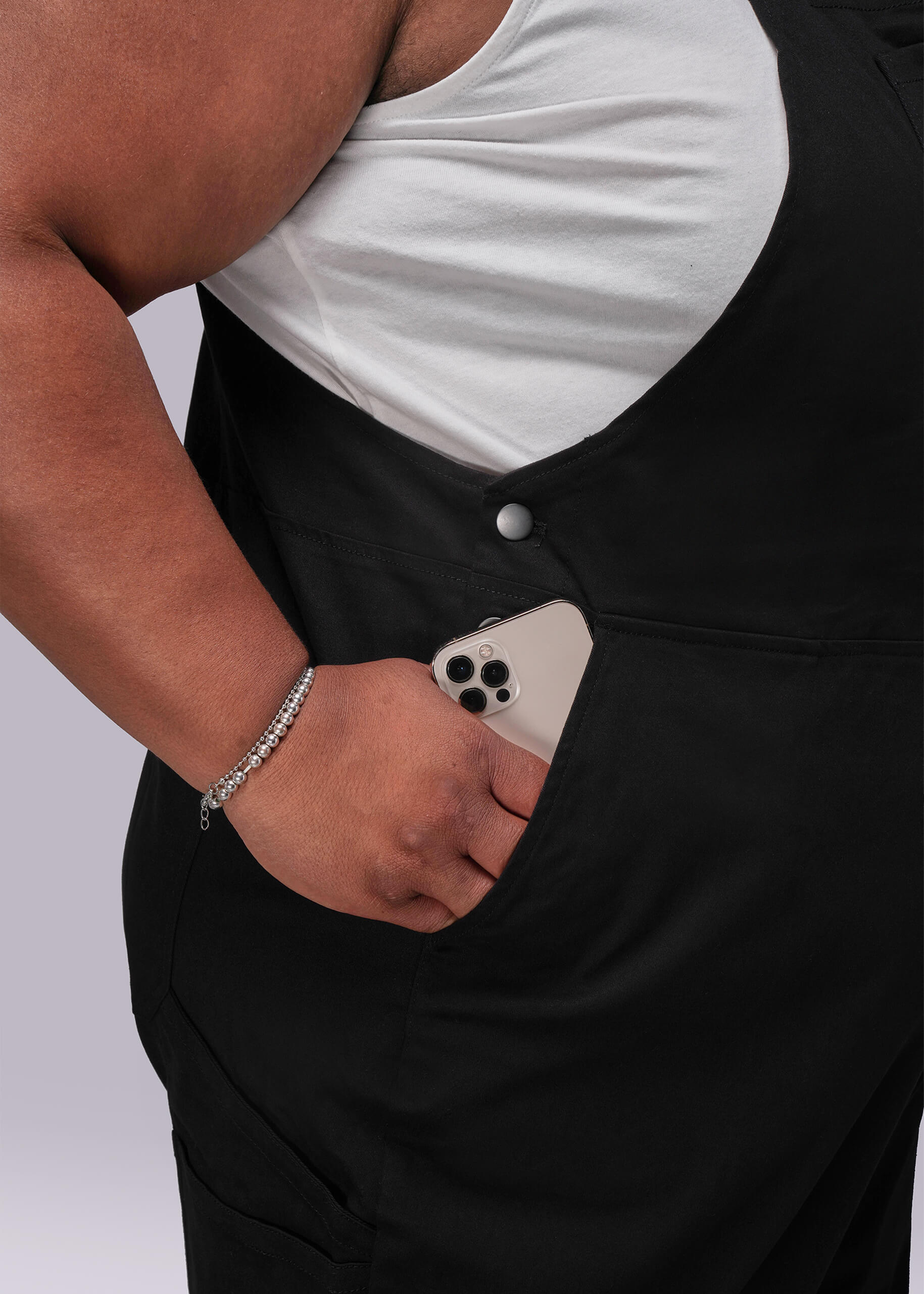 1X=Person wearing black overalls with a white shirt underneath, holding a phone in their pocket.