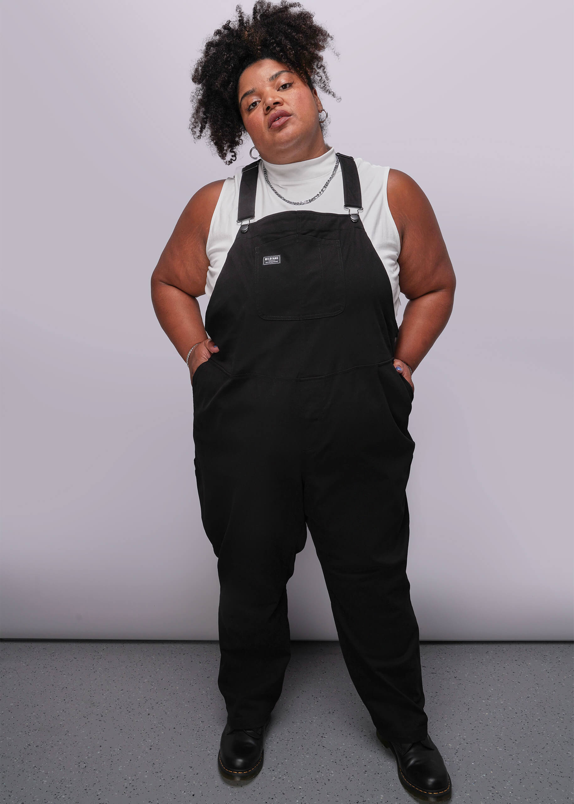 1X=Person wearing black overalls against a plain background