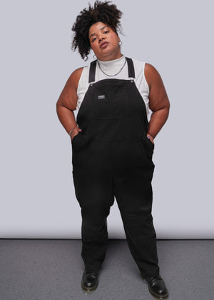 1X=Person wearing black overalls against a plain background