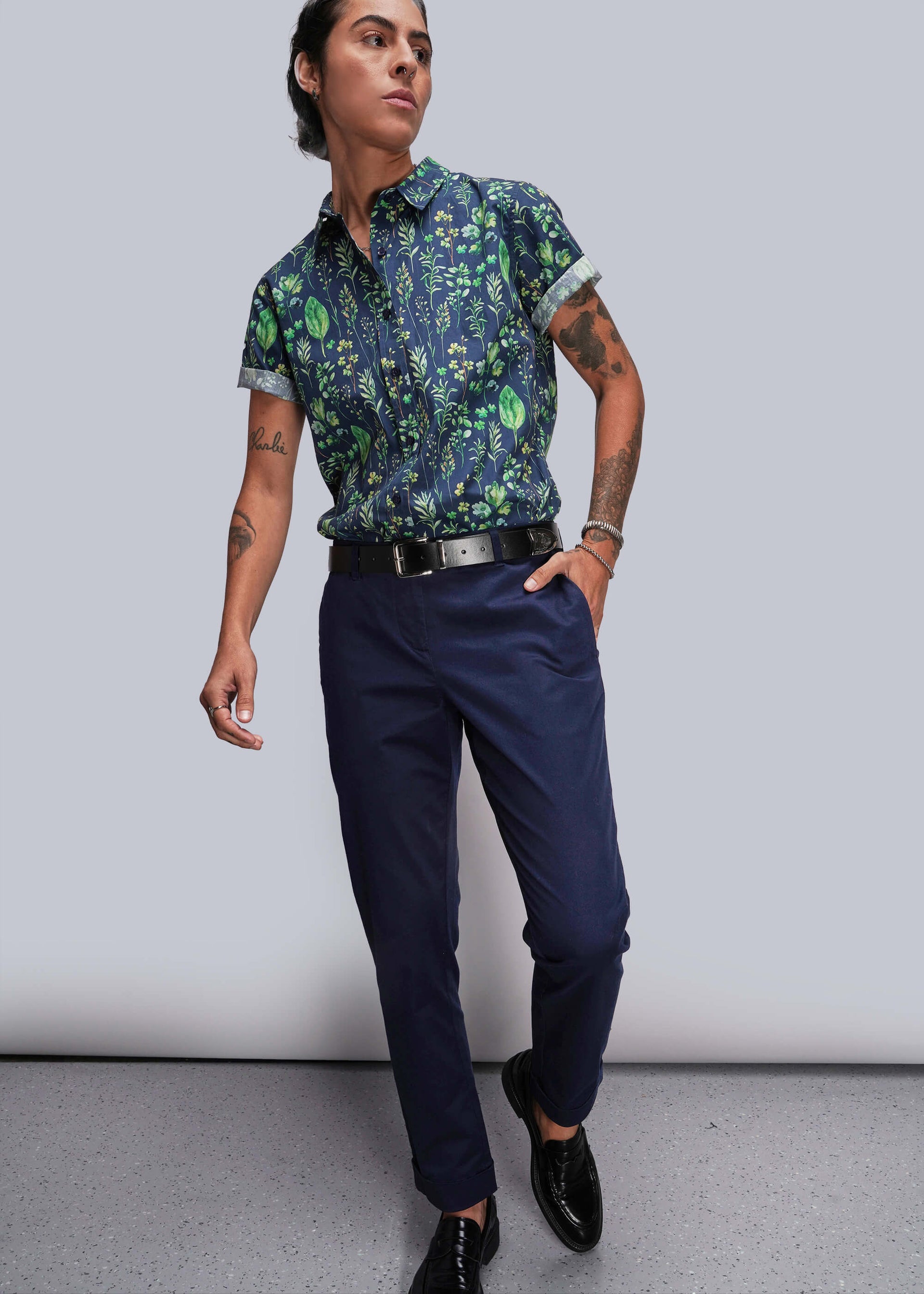 S=Person wearing a patterned shirt and navy pants against a plain background
