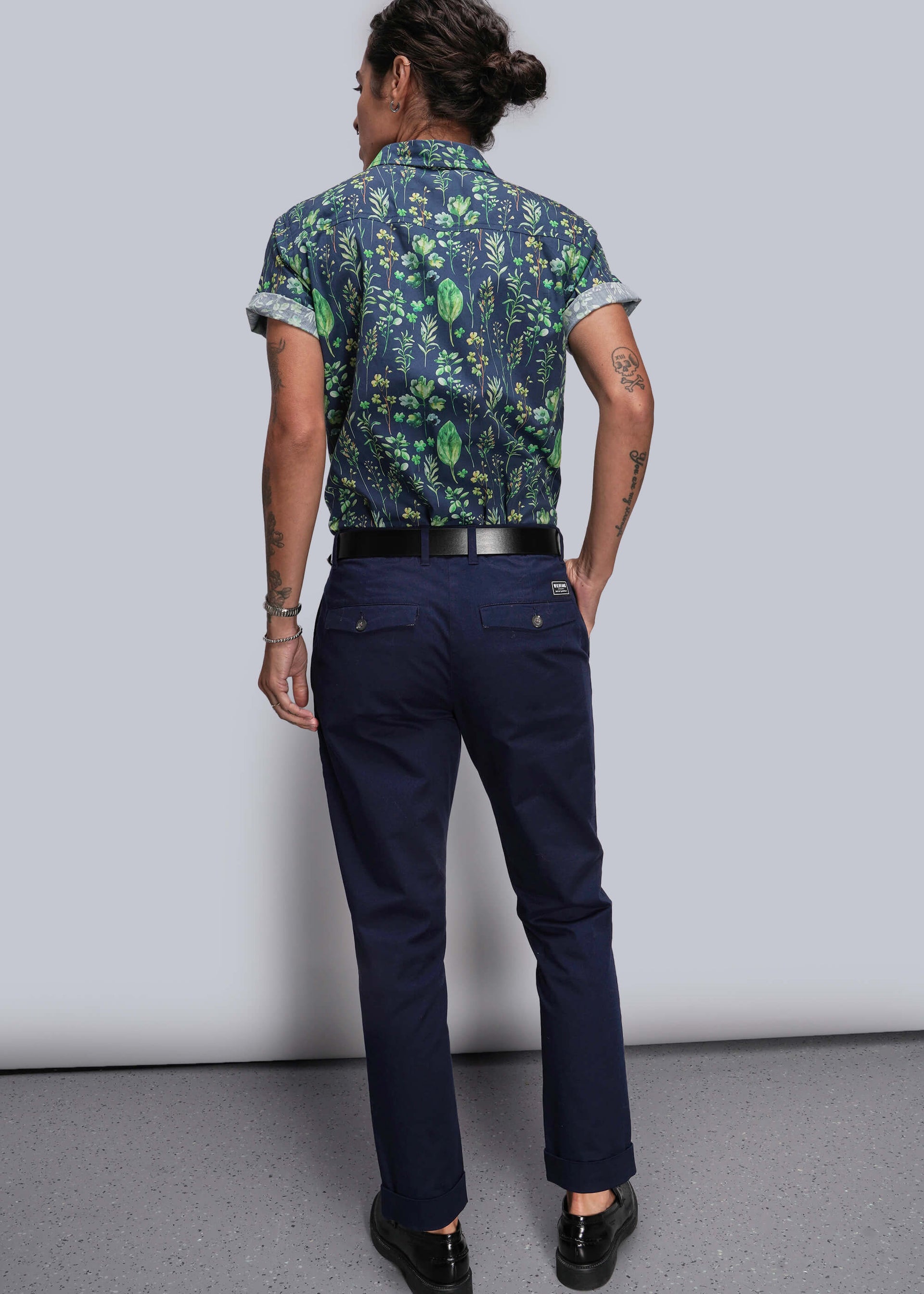 S=Person wearing a patterned shirt and navy pants against a plain background