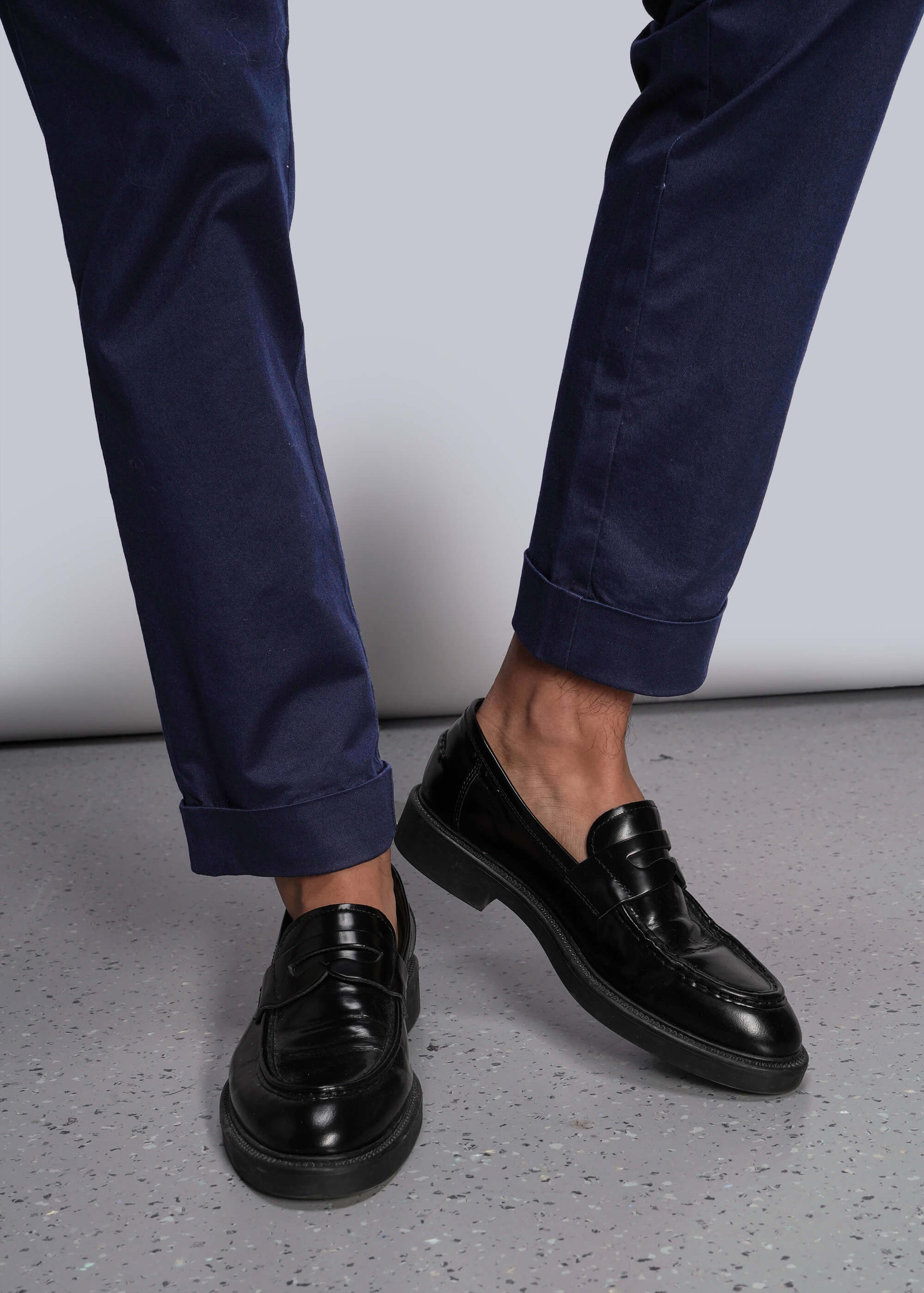S=Black dress shoes worn with navy pants on a light gray background