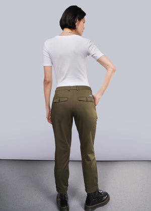 S=Rear view of a person with short dark hair against a white background, wearing a wardrobe staple: a white short-sleeved shirt, The Essential Trouser in classic olive green, and black shoes. They face away with one hand on their hip.