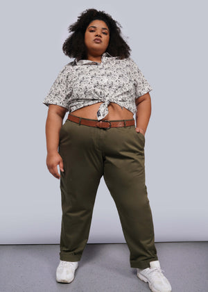 1X= A person stands confidently with one hand in their pocket, featuring a knotted patterned shirt, The Essential Trouser, and white sneakers. The plain background accentuates their bold stance and fashion-forward style, highlighting how these trousers are the ultimate wardrobe staple.