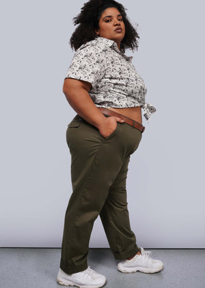 1X=A person wearing a patterned short-sleeve shirt, The Essential Trouser, and white sneakers stands with one hand in their pocket. They face sideways, confidently looking at the camera against a plain grey backdrop—a true wardrobe staple capturing effortless style.