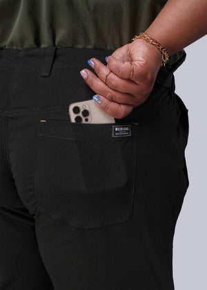 1X=Person wearing black pants with a visible brand label, holding a phone.