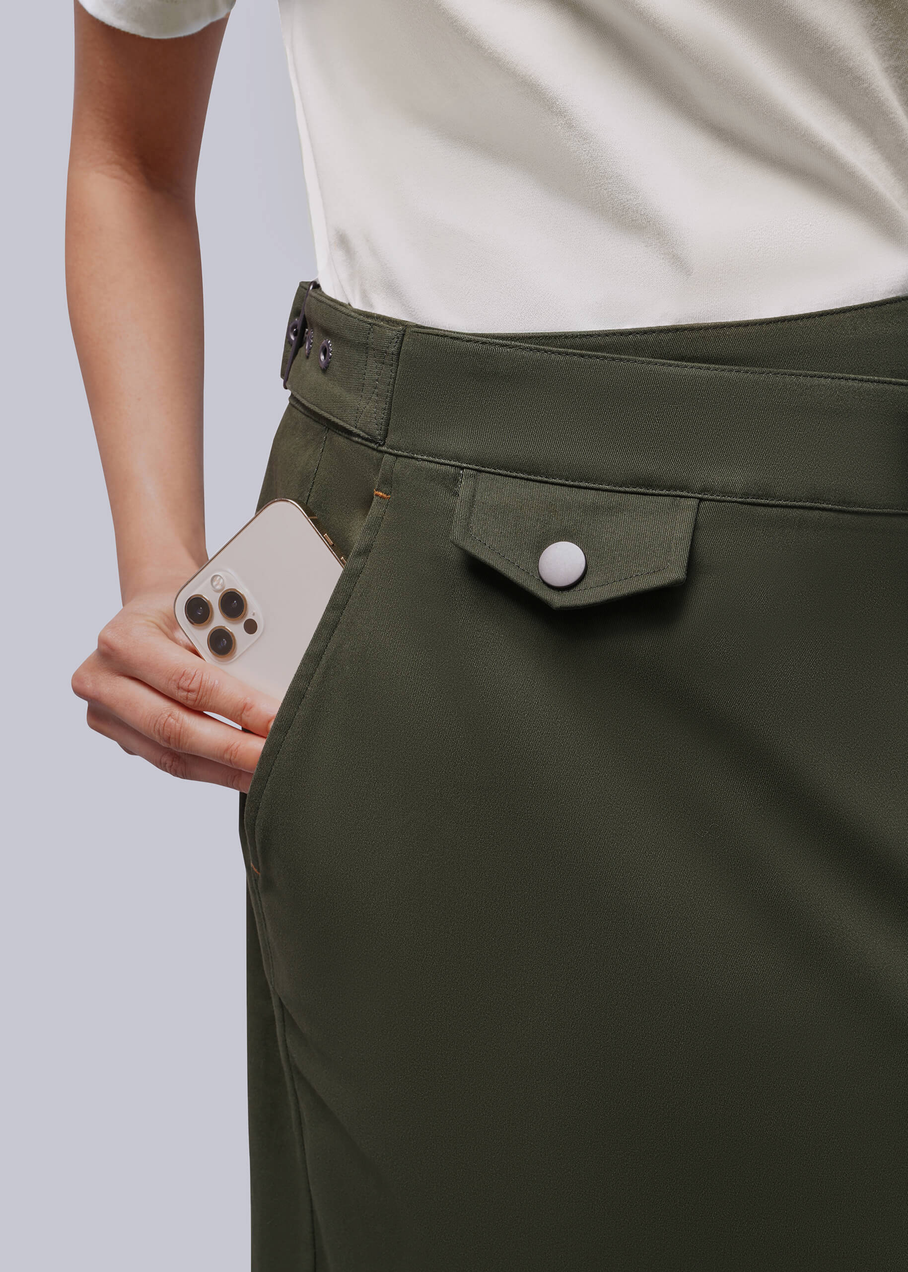 S=Close up of person placing phone in side pocket of gren skirt