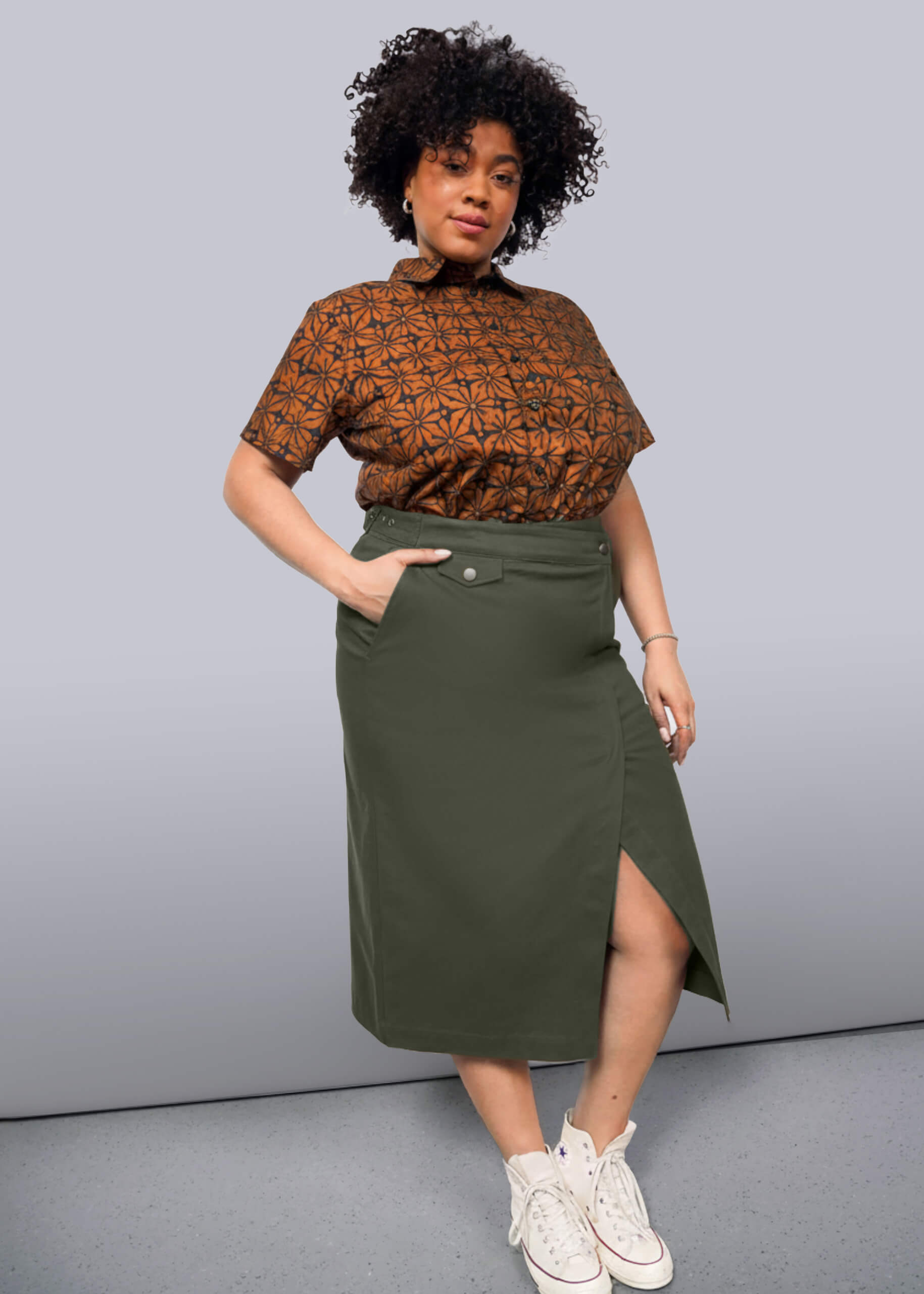 1X=Woman wearing a patterned top and green skirt against a gray background