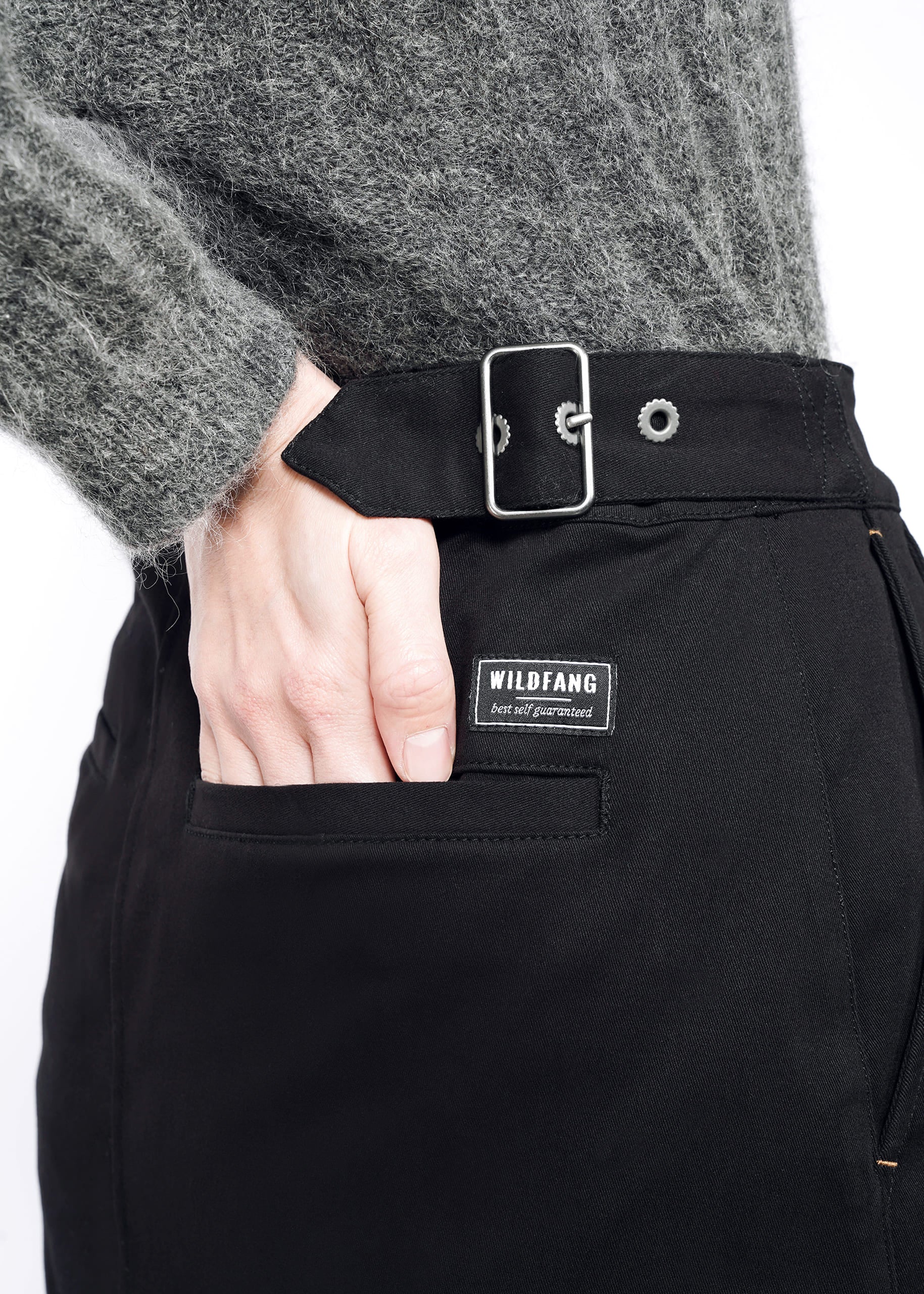 A person wears a fuzzy gray sweater and The Essential Utility Wrap Skirt, which features an adjustable waistband and a WILDFANG label above the front pocket, with their hand resting in the pocket.