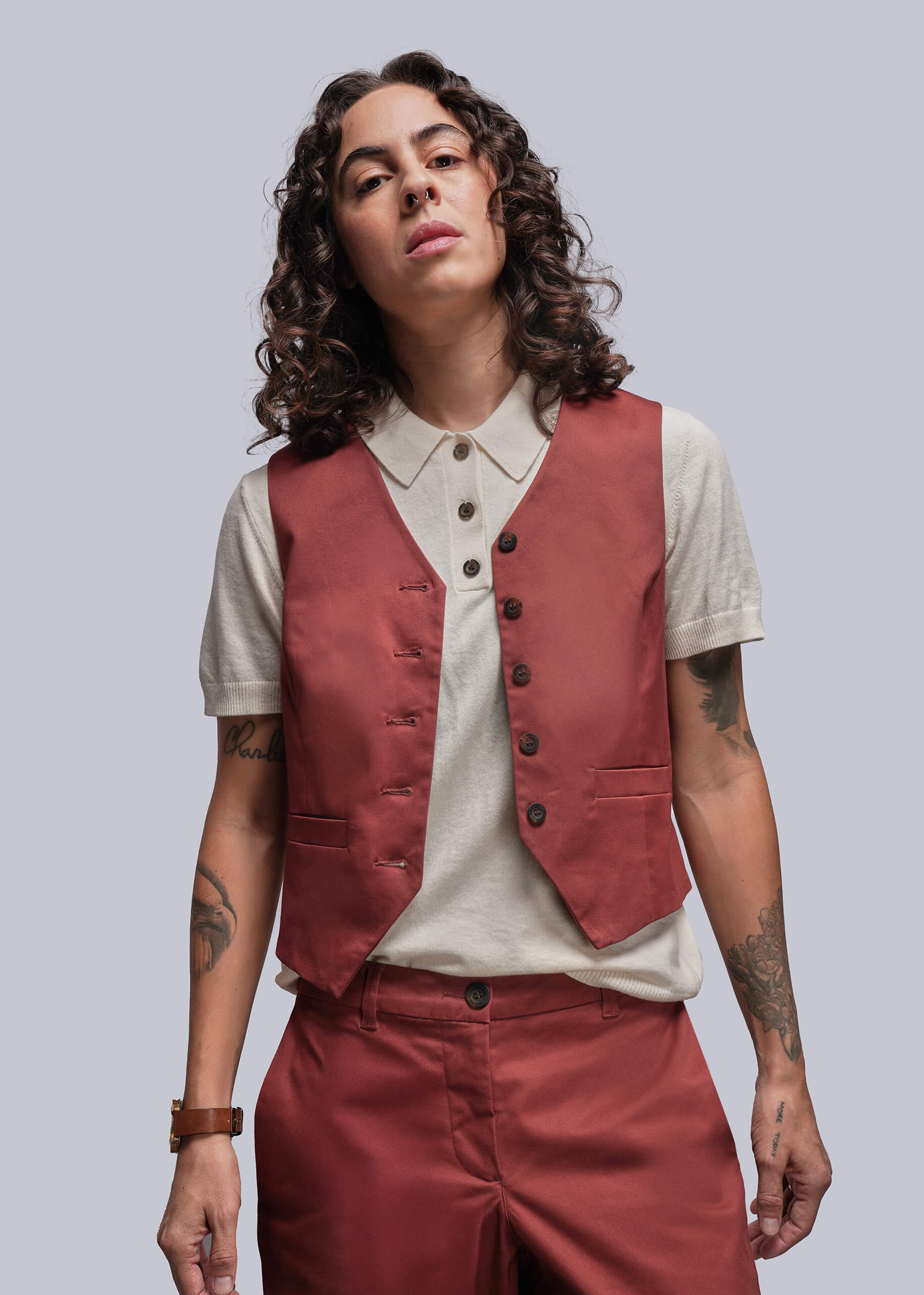 S=Person wearing a rust colored vest over a white sweater polo with a plain background