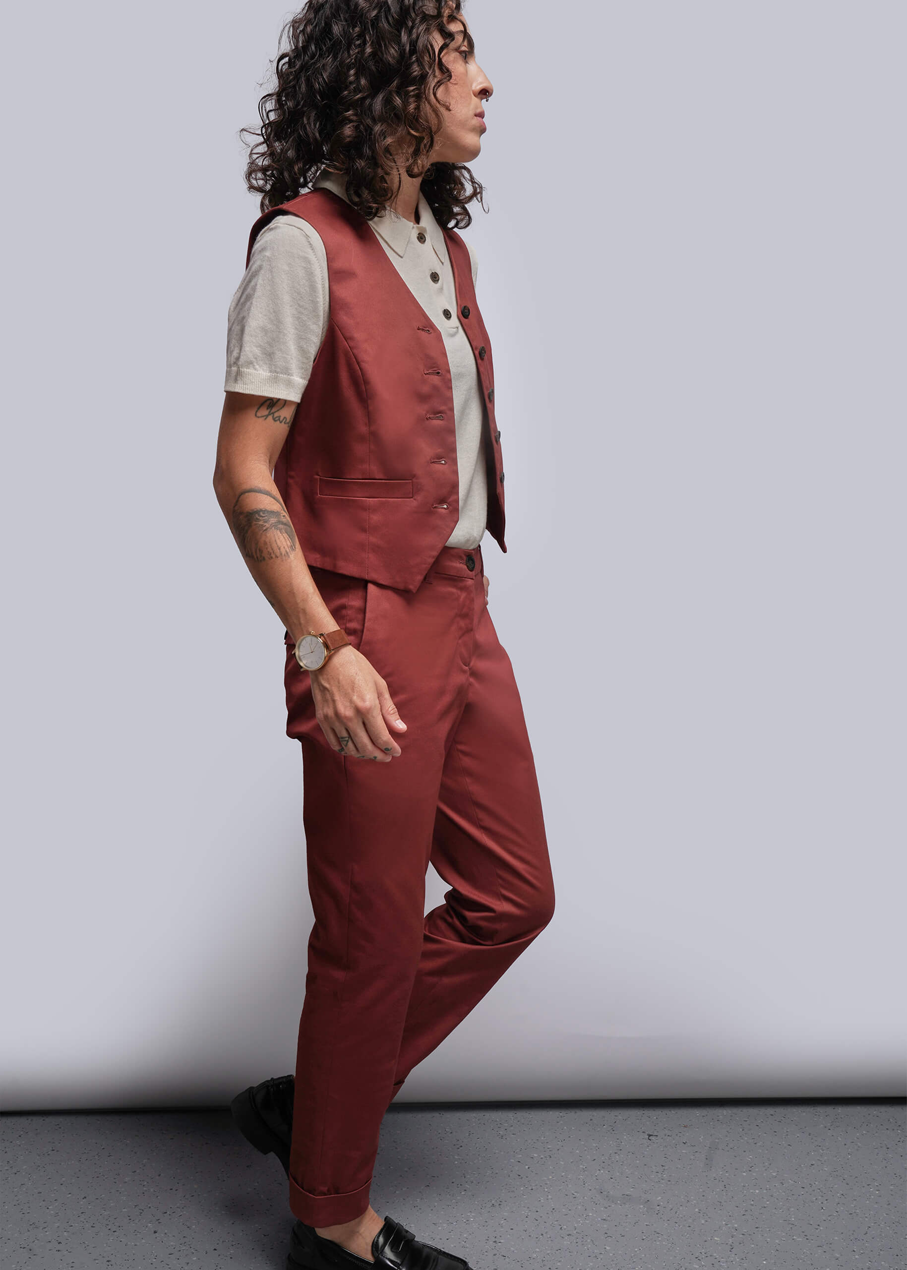 S=Person wearing a  rust colored  vest and pants against a plain background