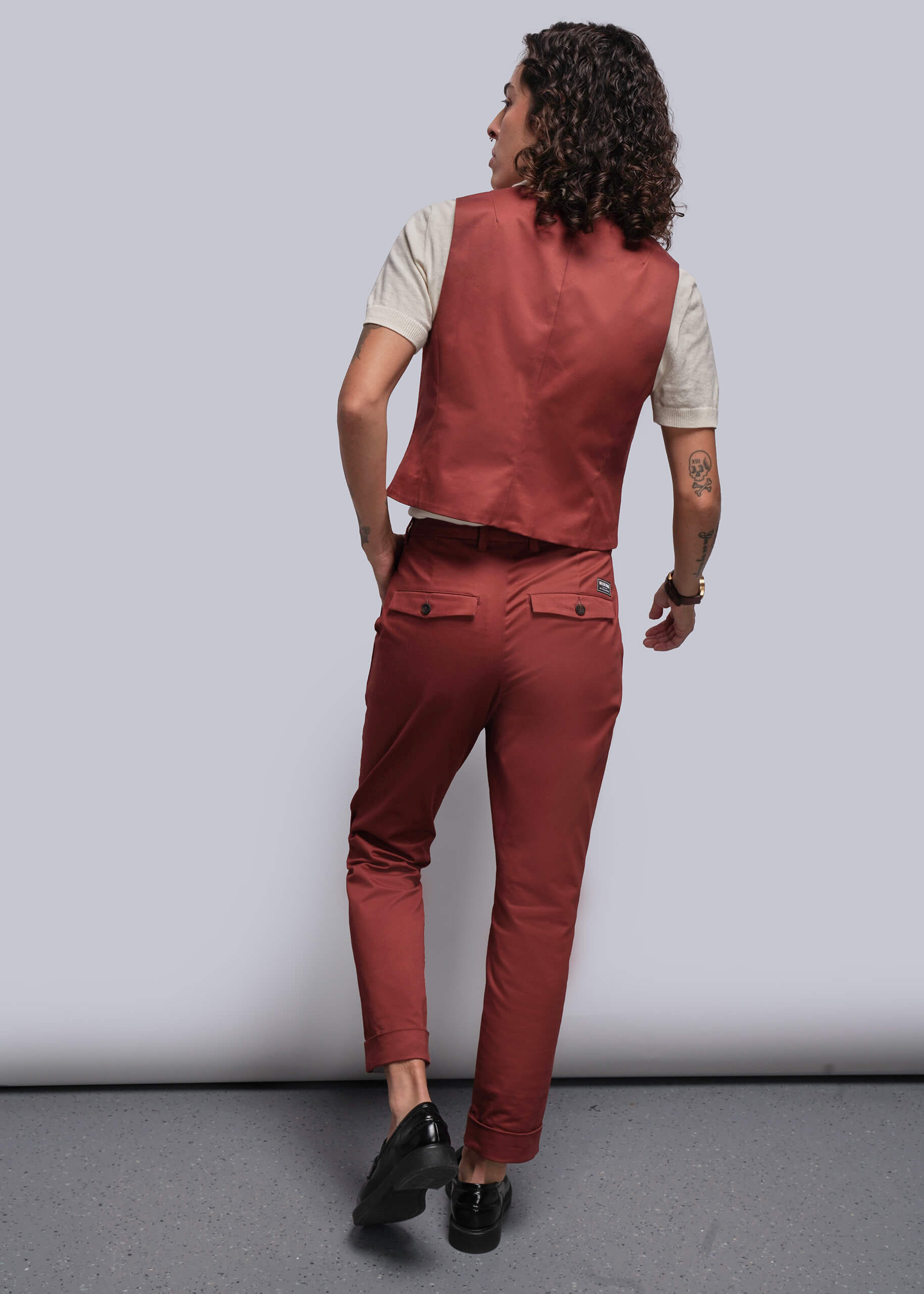 S=Person wearing a  rust colored vest and pants against a plain background
