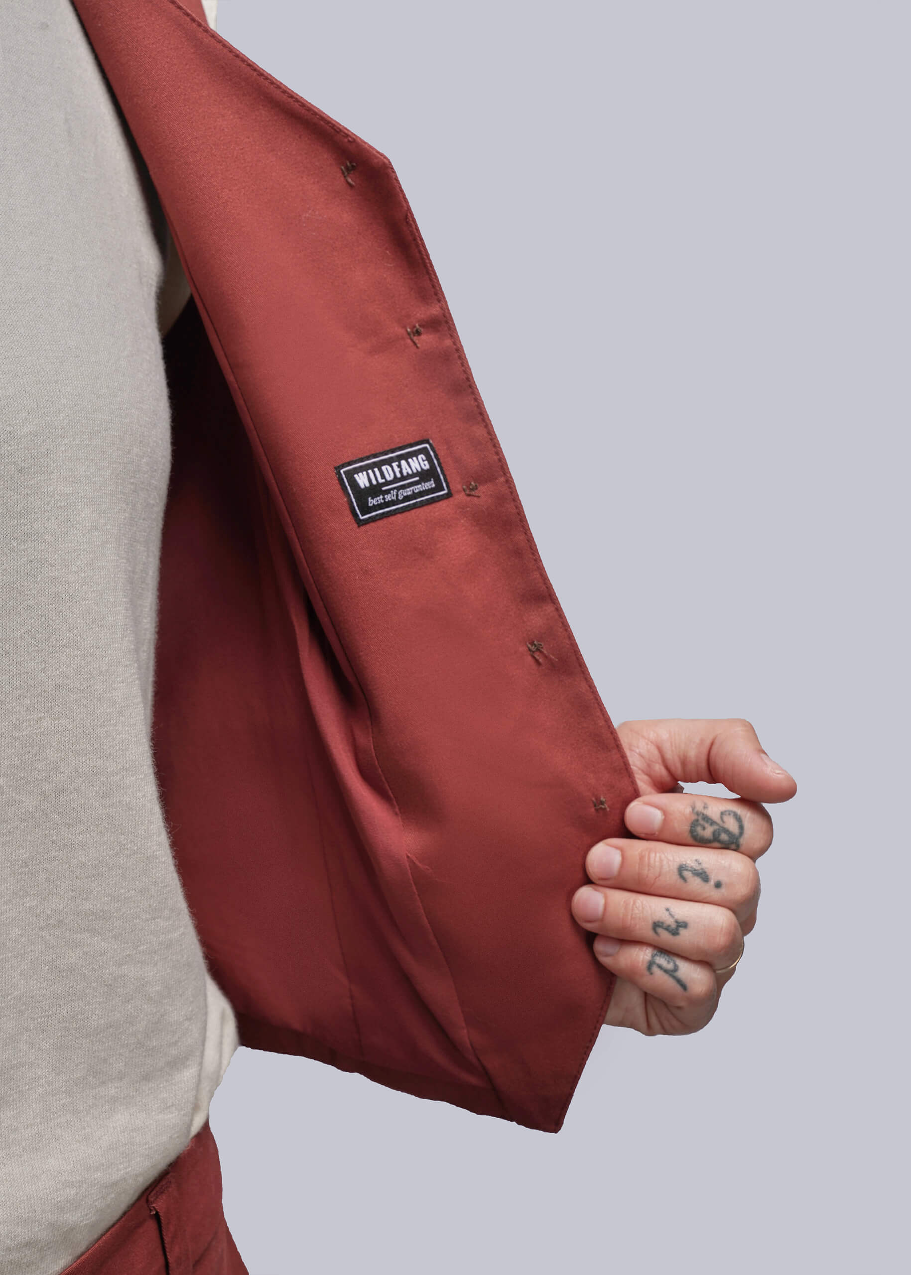 S=Person wearing a  rust colored  jacket with a visible Wildfang brand logo patch on a plain background