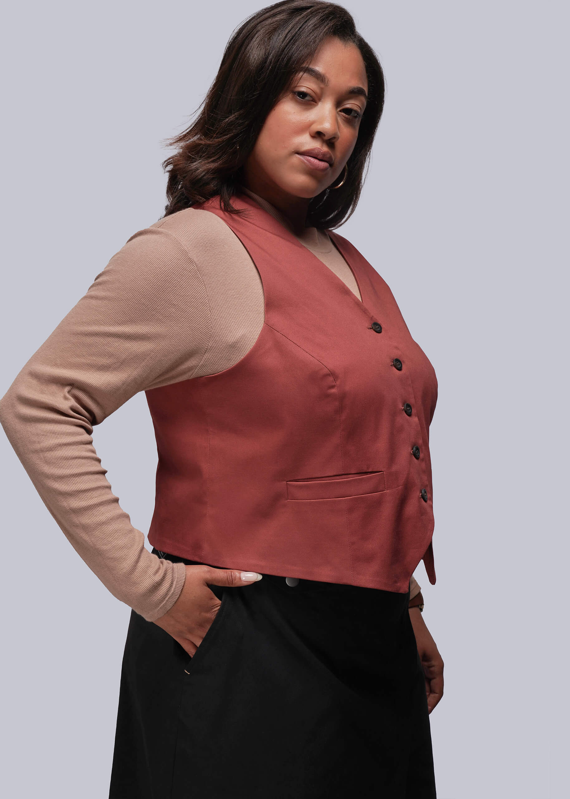 1X=Person wearing a rust colored vest over a beige long-sleeve shirt on a gray background