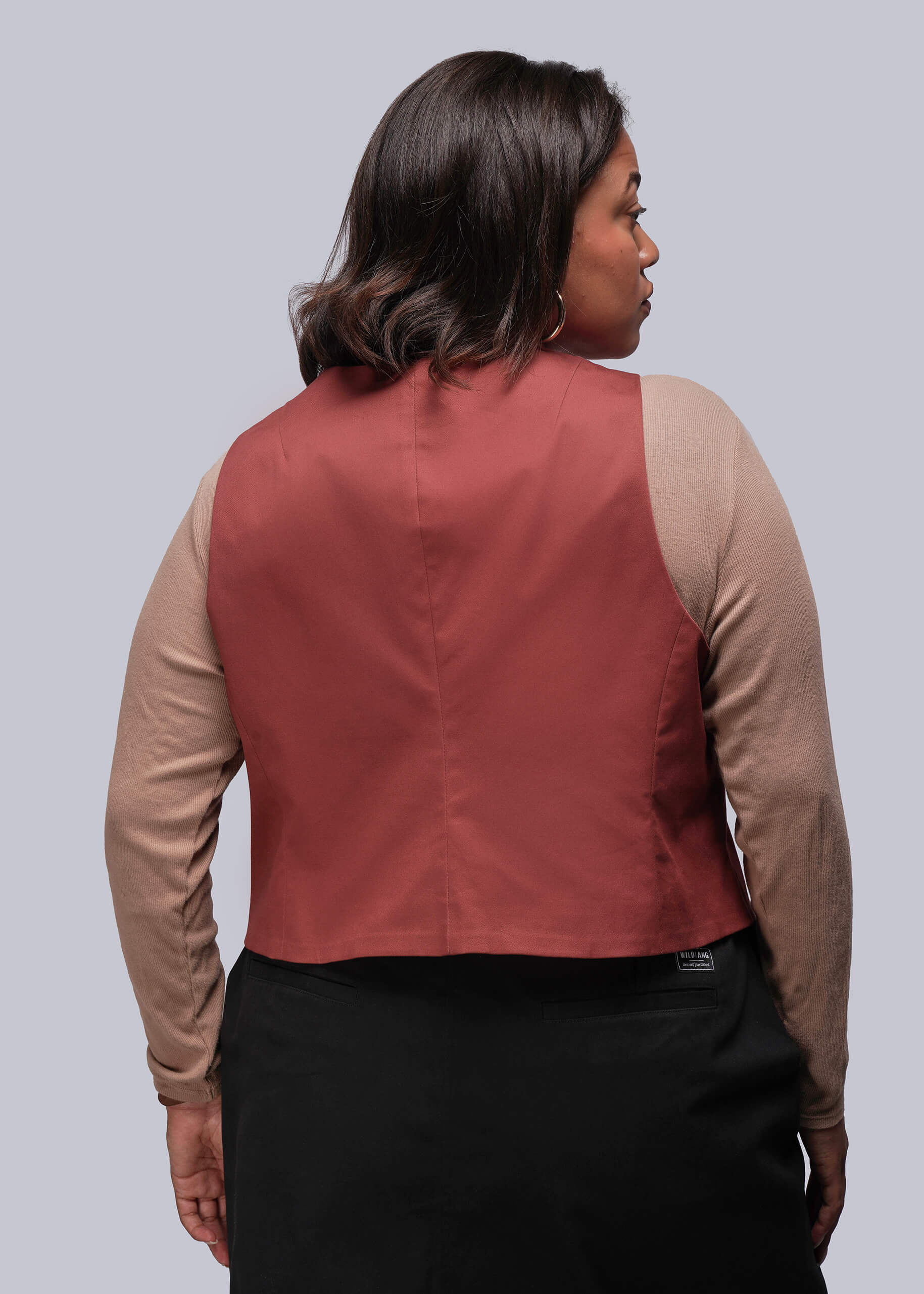 1X=Back of person wearing a rust colored vest over a beige long-sleeve shirt on a gray background