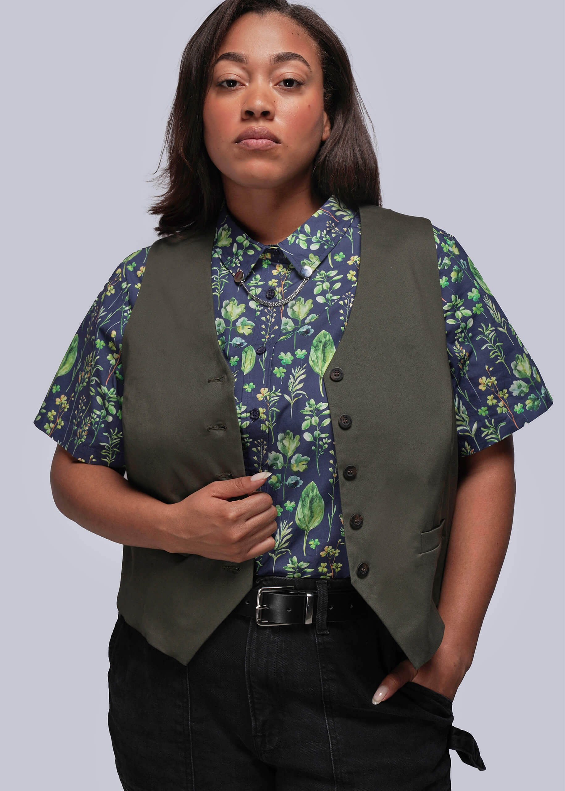 1X=Person wearing a green vest over a leaf print shirt on a gray background