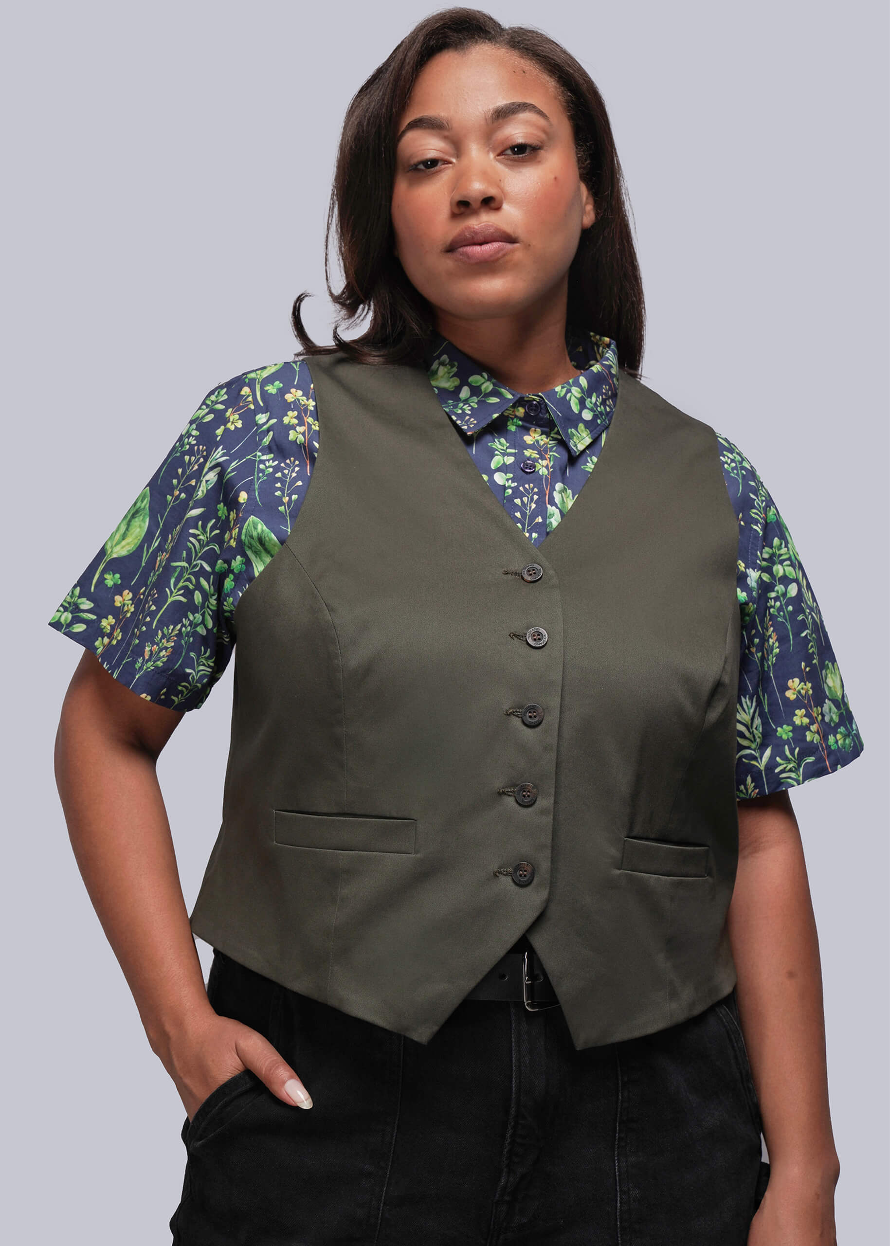 1X=Person wearing a green vest over a leaf print shirt on a gray background
