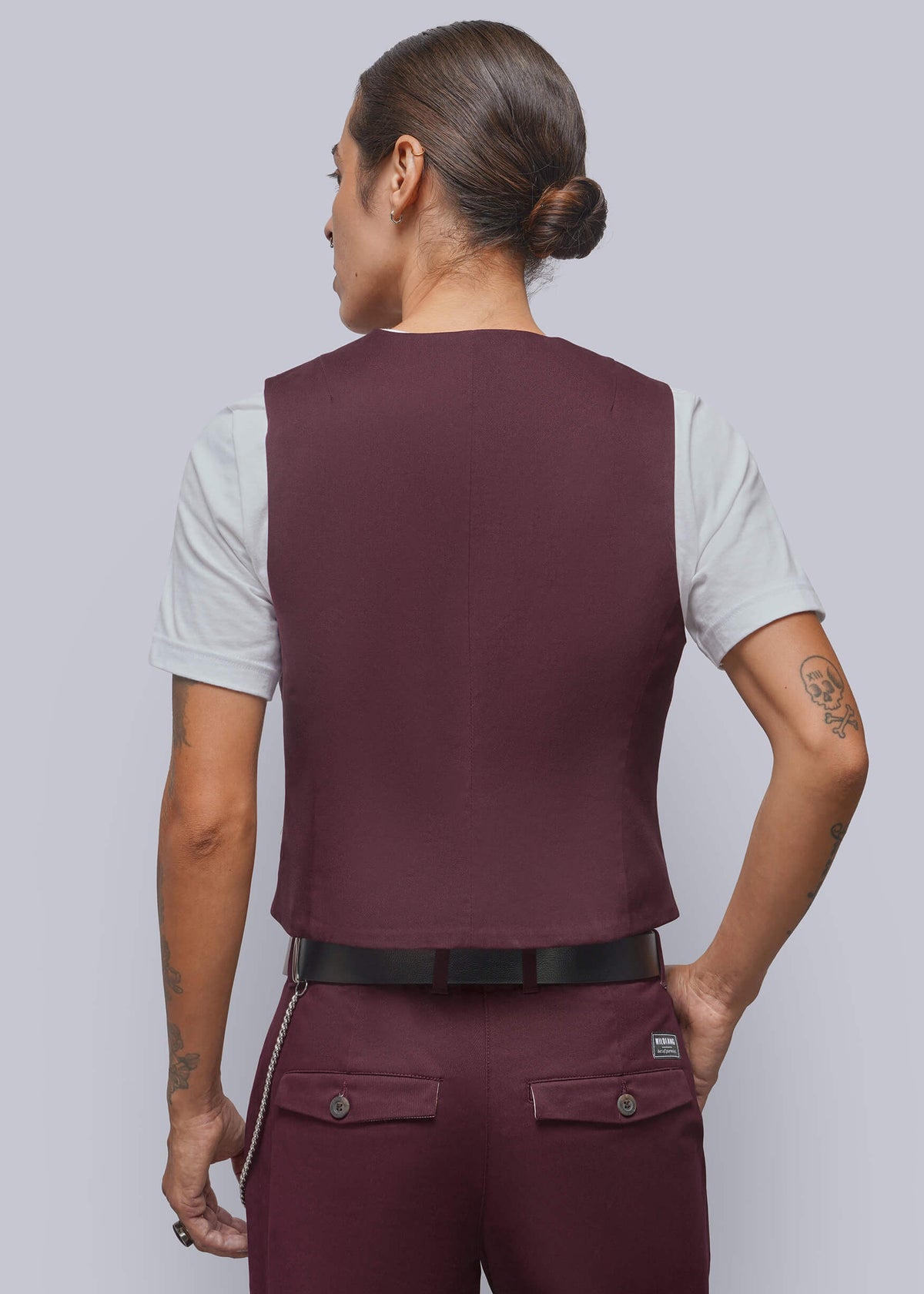 S=A person shown from the back wearing a sleeveless burgundy vest over a white t-shirt, paired with matching burgundy trousers and a black belt, against a solid gray background.