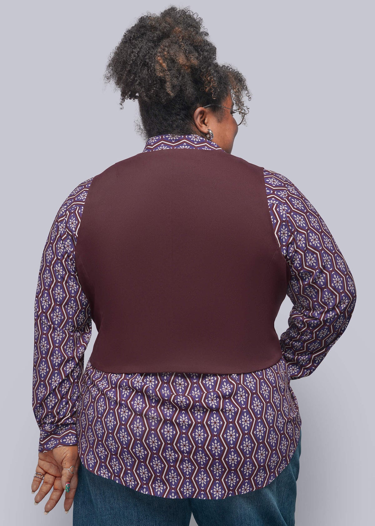 1X=A person shown from the back wearing a solid dark burgundy vest layered over a purple and blue patterned button-down shirt, paired with blue jeans, against a solid gray studio background.