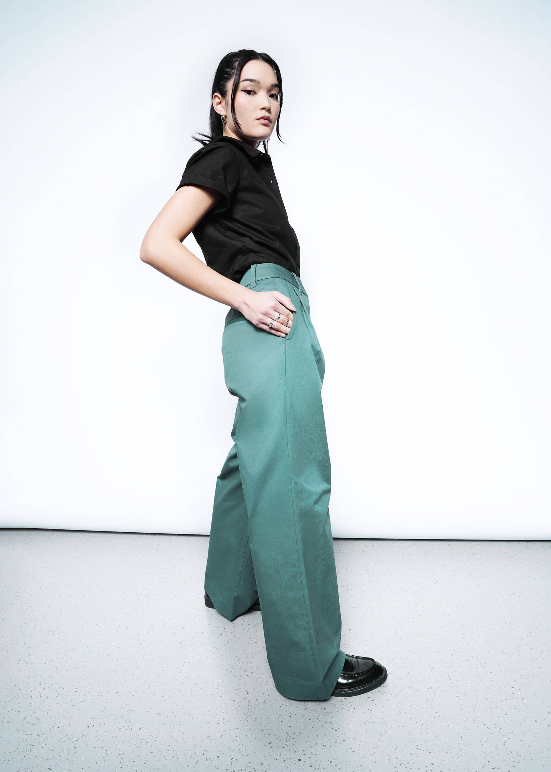 Side full body view of model in Wildfang Essential Wide Leg Trouser in Dark Teal paired with black short sleeve button up