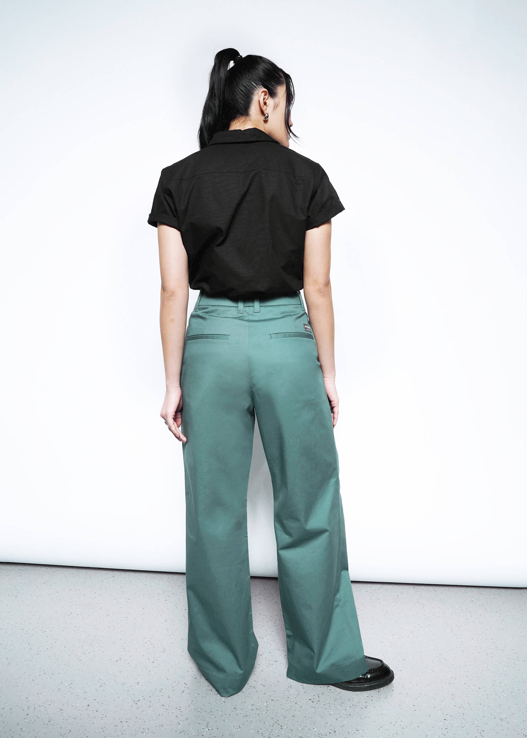 Full body back view of model in Wildfang Essential Wide Leg Trouser in Dark Teal, showcasing welted back pockets