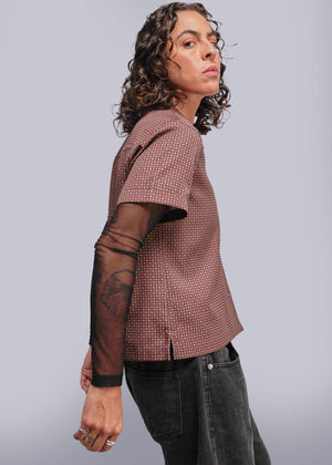 S=Person wearing a patterned top with sheer sleeves against a plain background