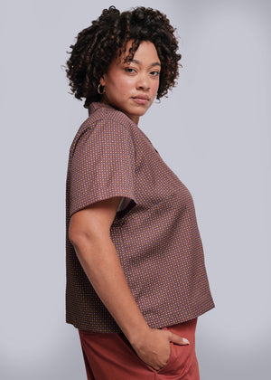 1X=Woman wearing a brown patterned shirt against a gray background