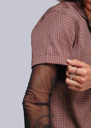 S=Close-up of a person wearing a patterned shirt with a neutral background