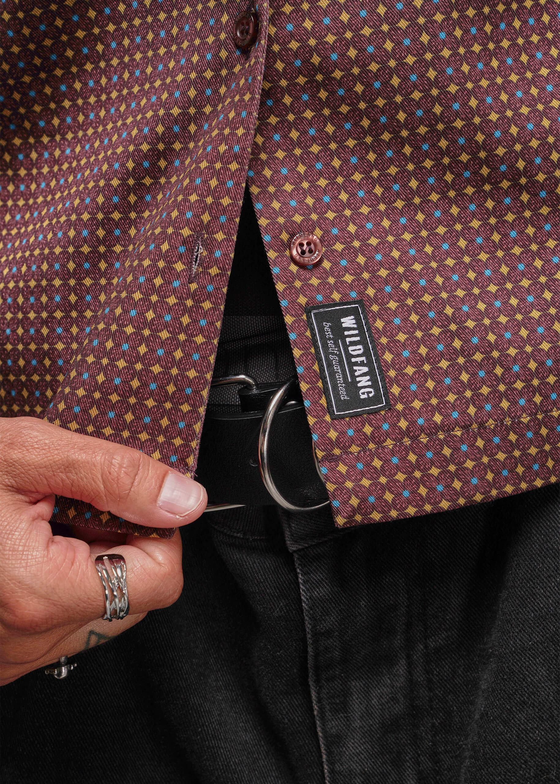 S=Close-up of a patterned shirt with a visible brand label, held by a hand.