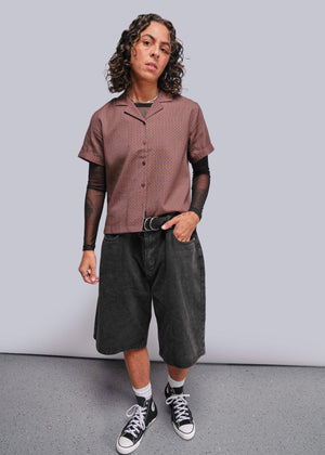 S=Person wearing a patterned shirt, dark shorts, and black sneakers on a plain background