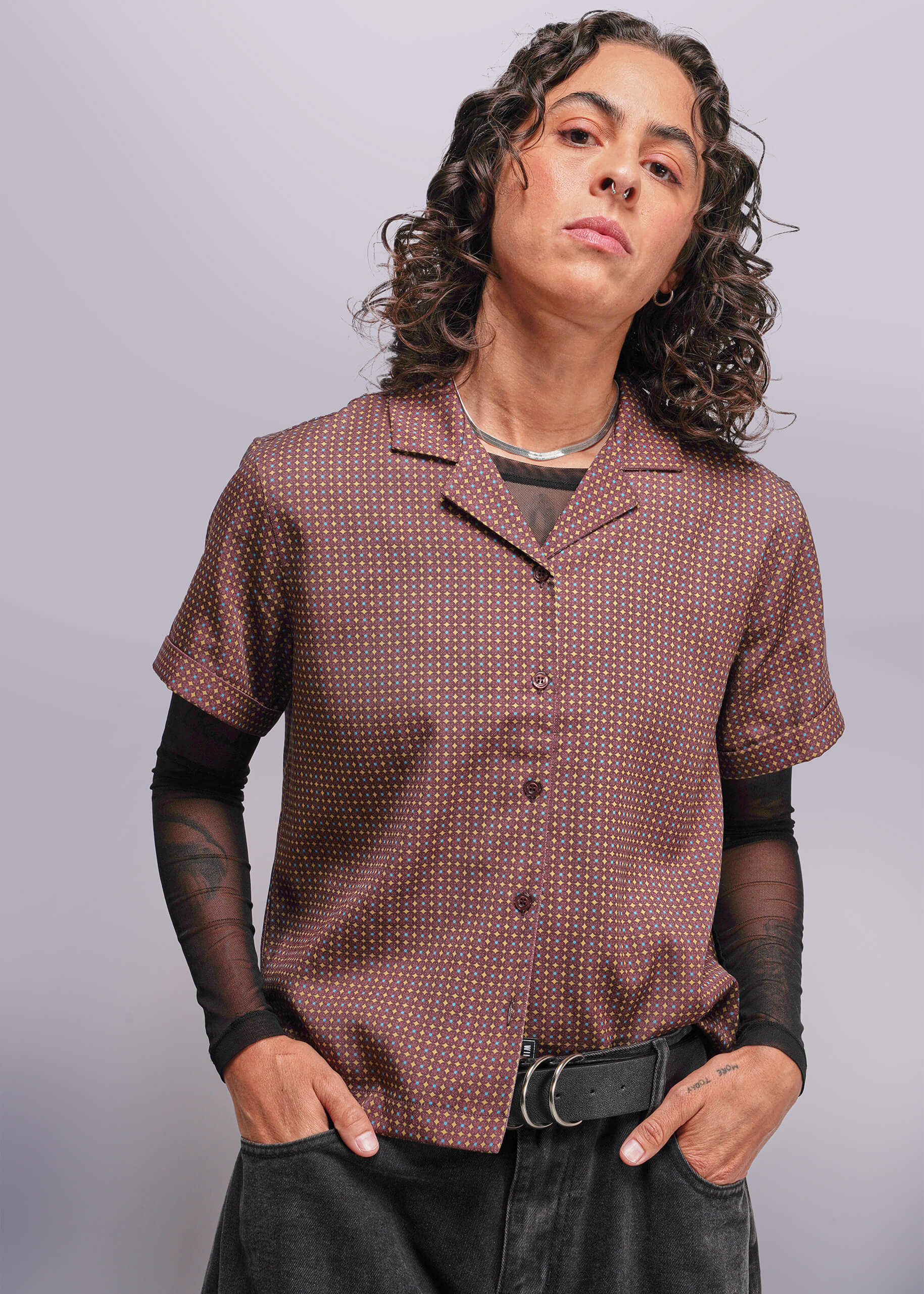 S=Person wearing a patterned brown shirt with black sleeves and pants against a plain background