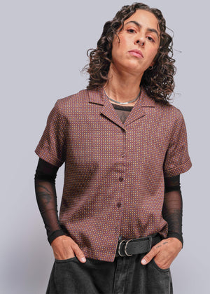 S=Person wearing a patterned brown shirt with black sleeves and pants against a plain background