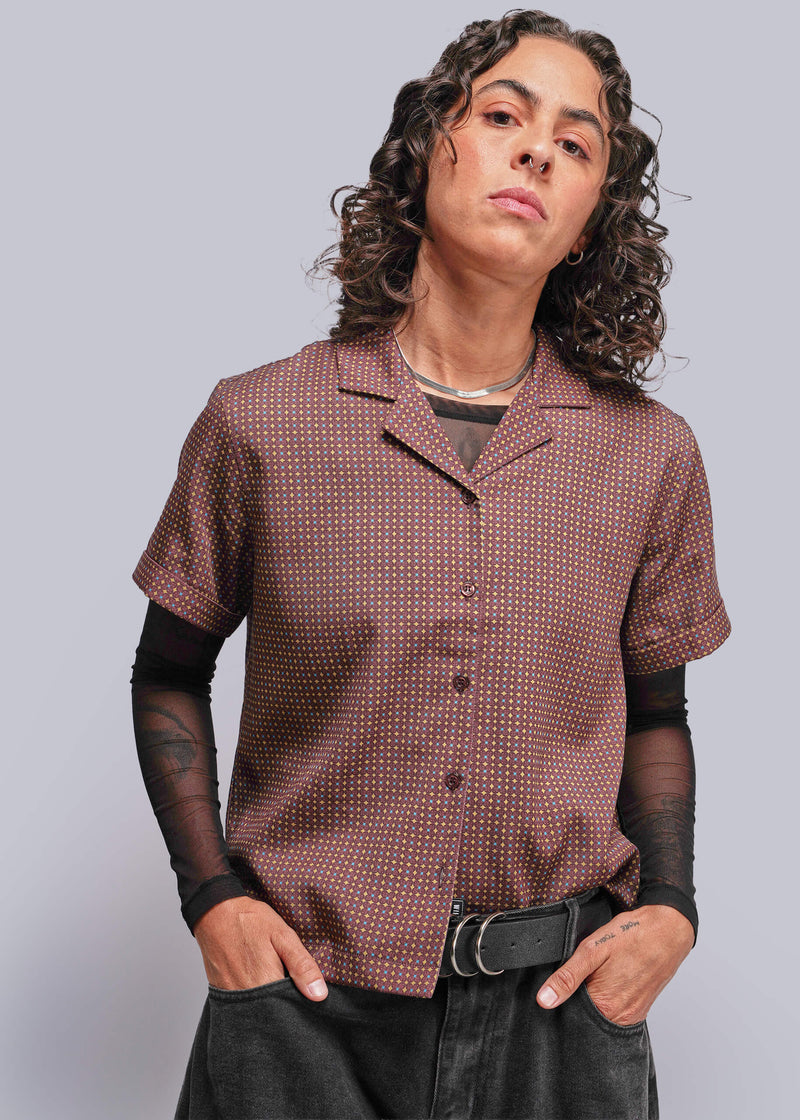 S=Person wearing a patterned brown shirt with black sleeves and pants against a plain background