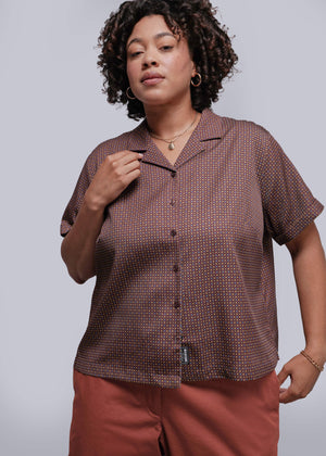 1X=Woman wearing a brown patterned button up against a plain background