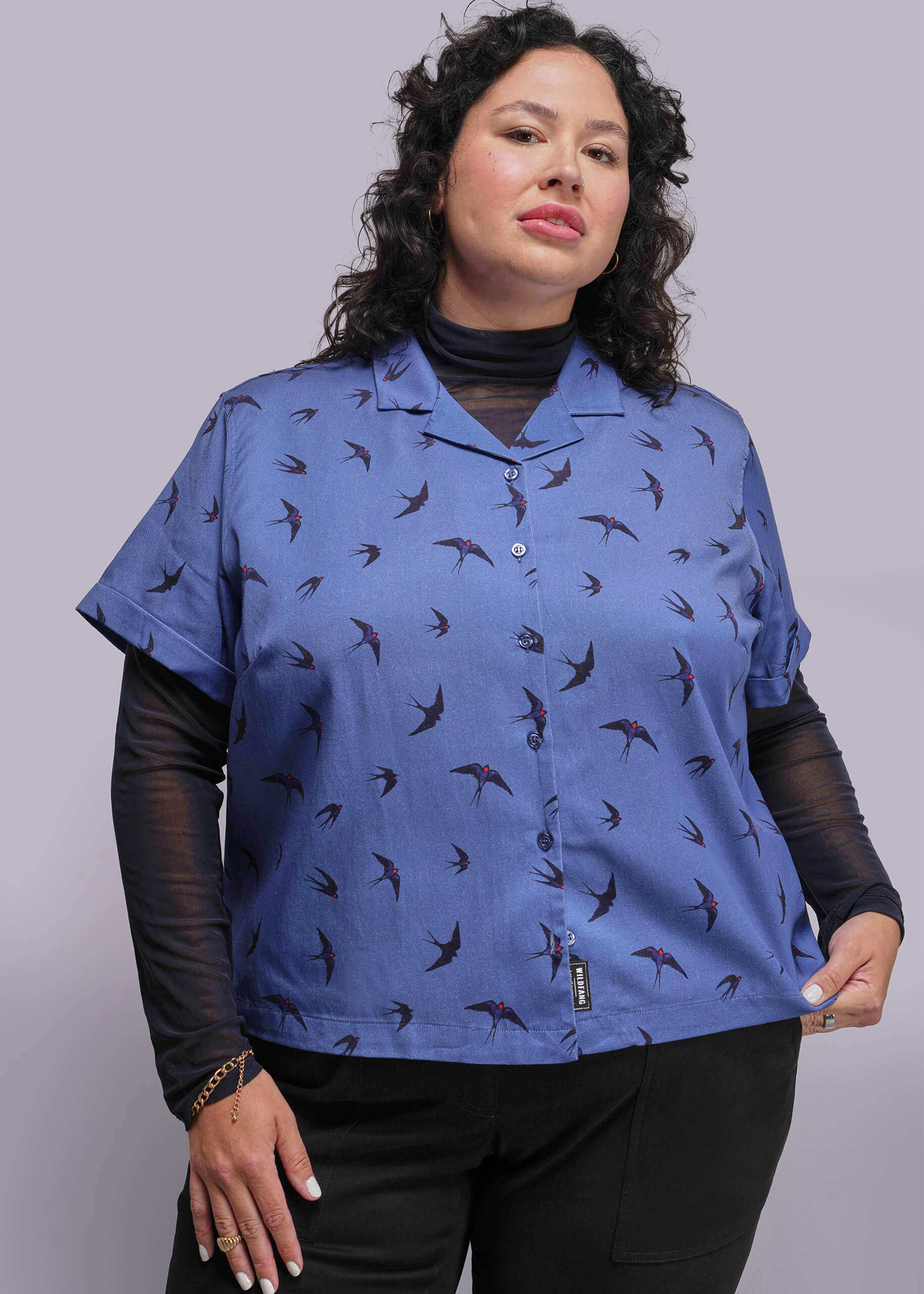 1X=Woman wearing a blue patterned shirt with black sleeves against a gray background