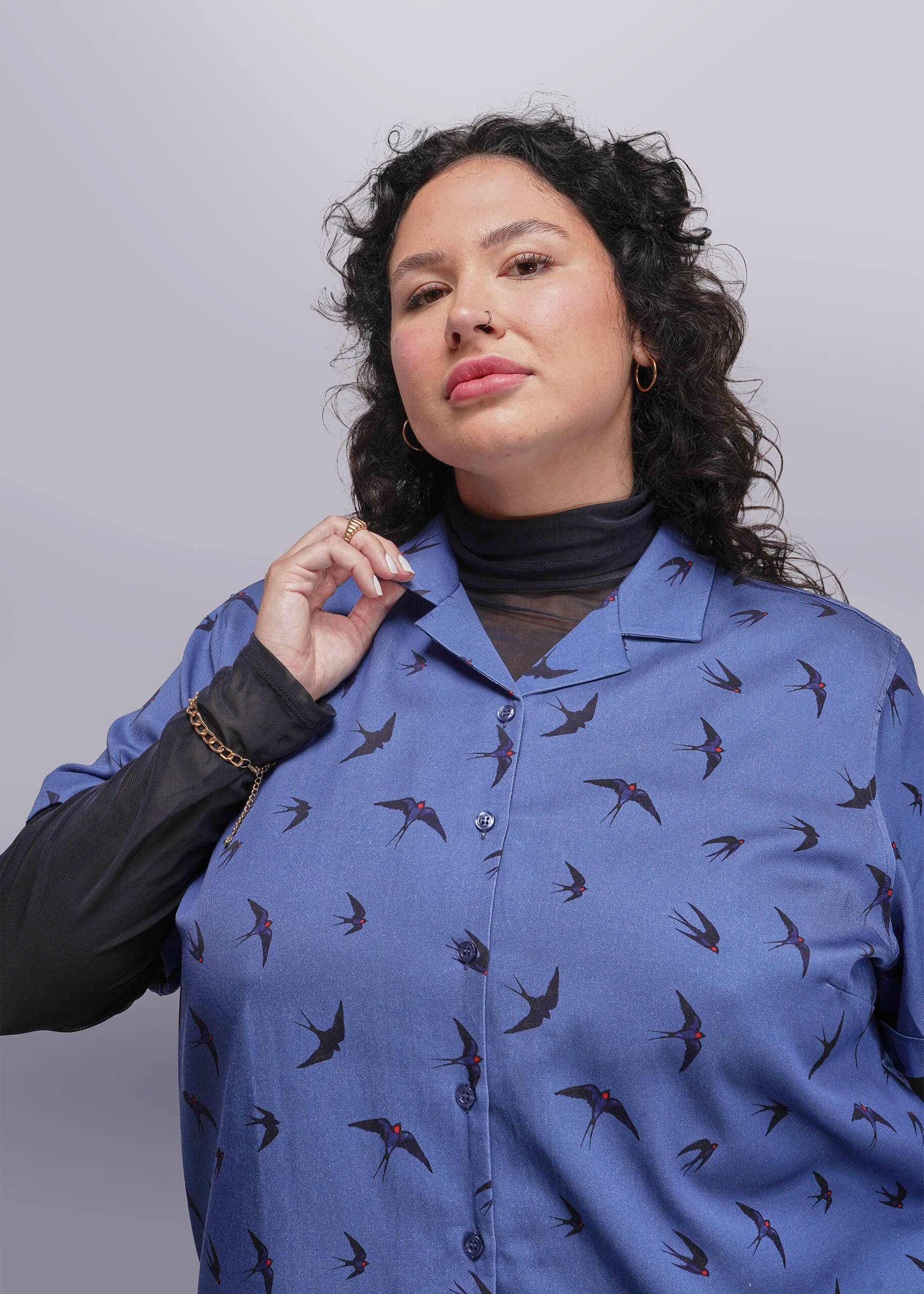 1X=Woman wearing a blue shirt with bird pattern against a gray background
