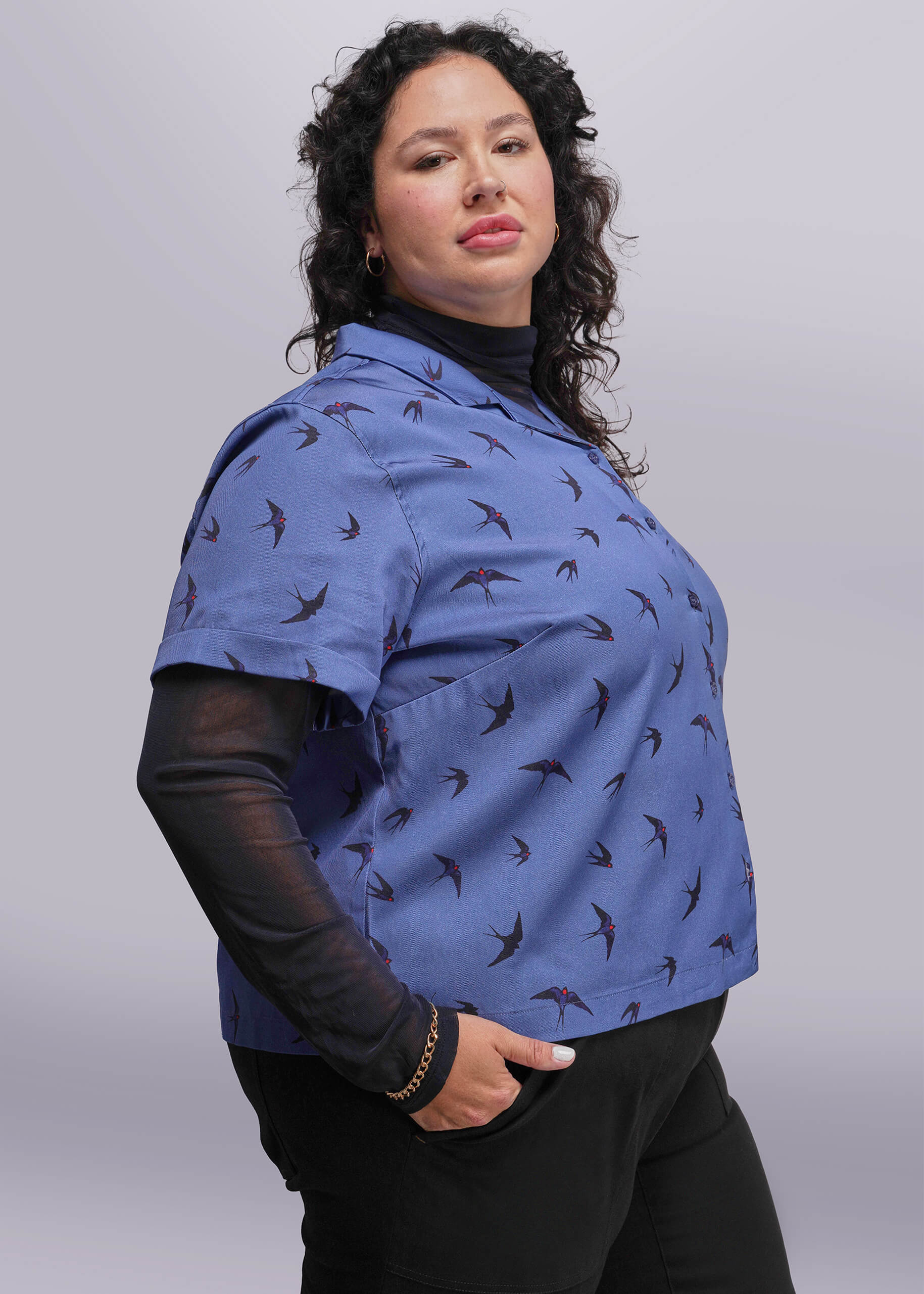 1X=Woman wearing a blue patterned shirt with black sleeves against a plain background