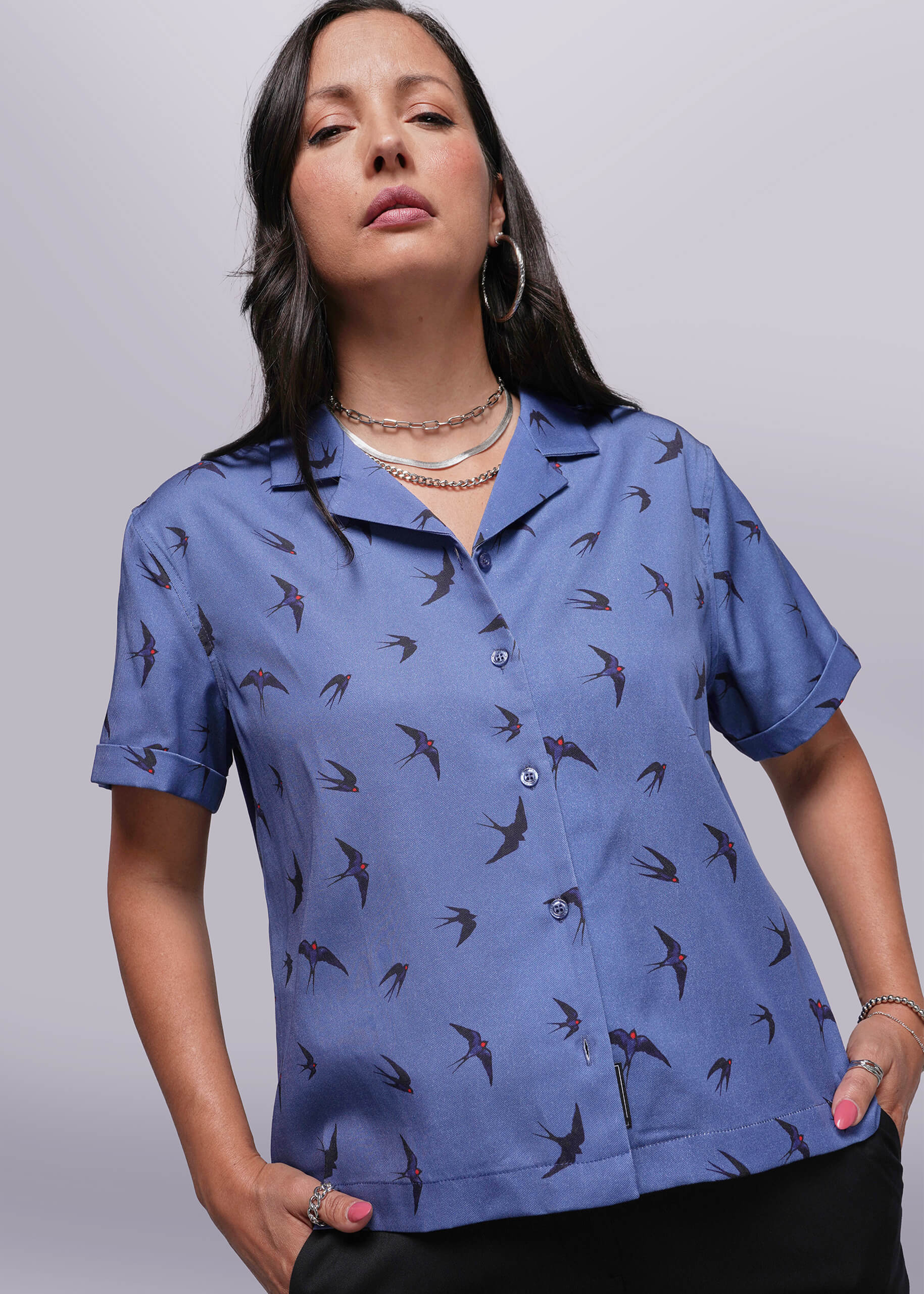 S=Woman wearing a blue shirt with bird pattern against a plain background