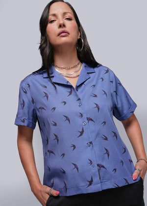 S=Woman wearing a blue shirt with bird pattern against a plain background