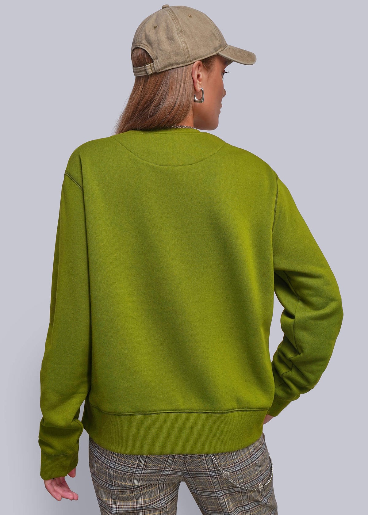 S=A person shown from the back wearing a green crewneck sweatshirt, a beige baseball cap, and plaid pants, set against a solid light gray background.