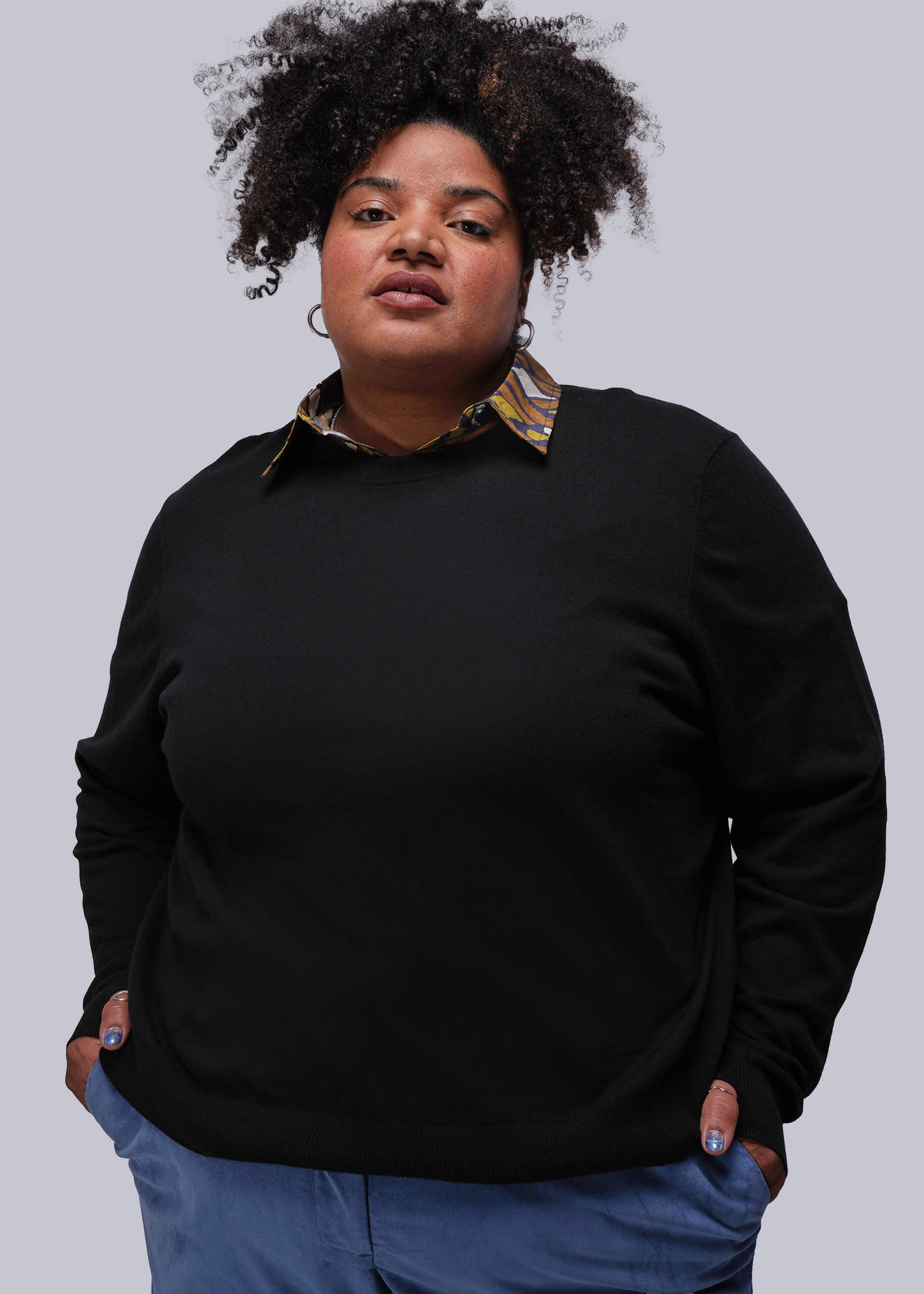 1X=Person wearing a black sweater over a patterned shirt with blue pants on a white background