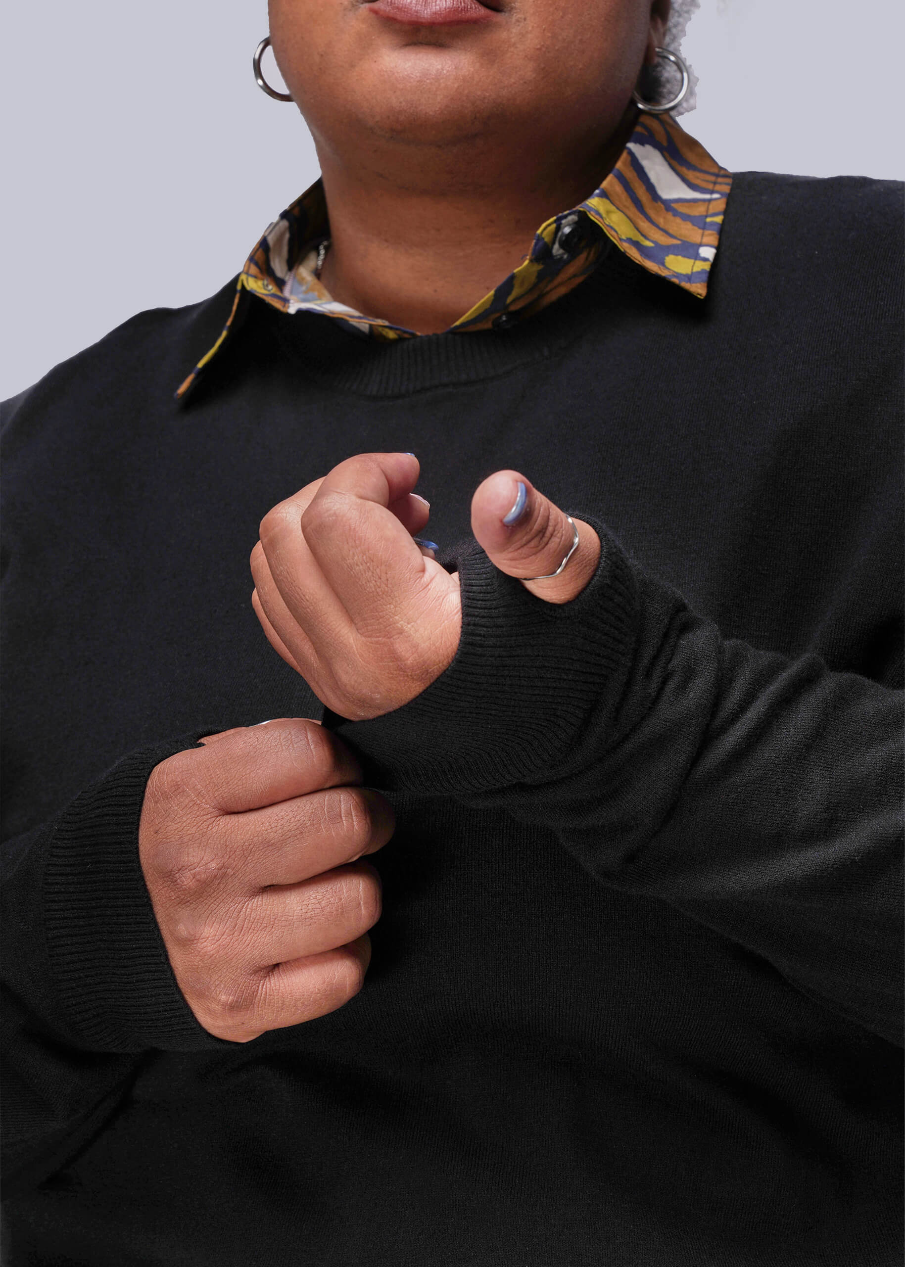 1X=Person wearing a black sweater over a patterned shirt with a neutral background