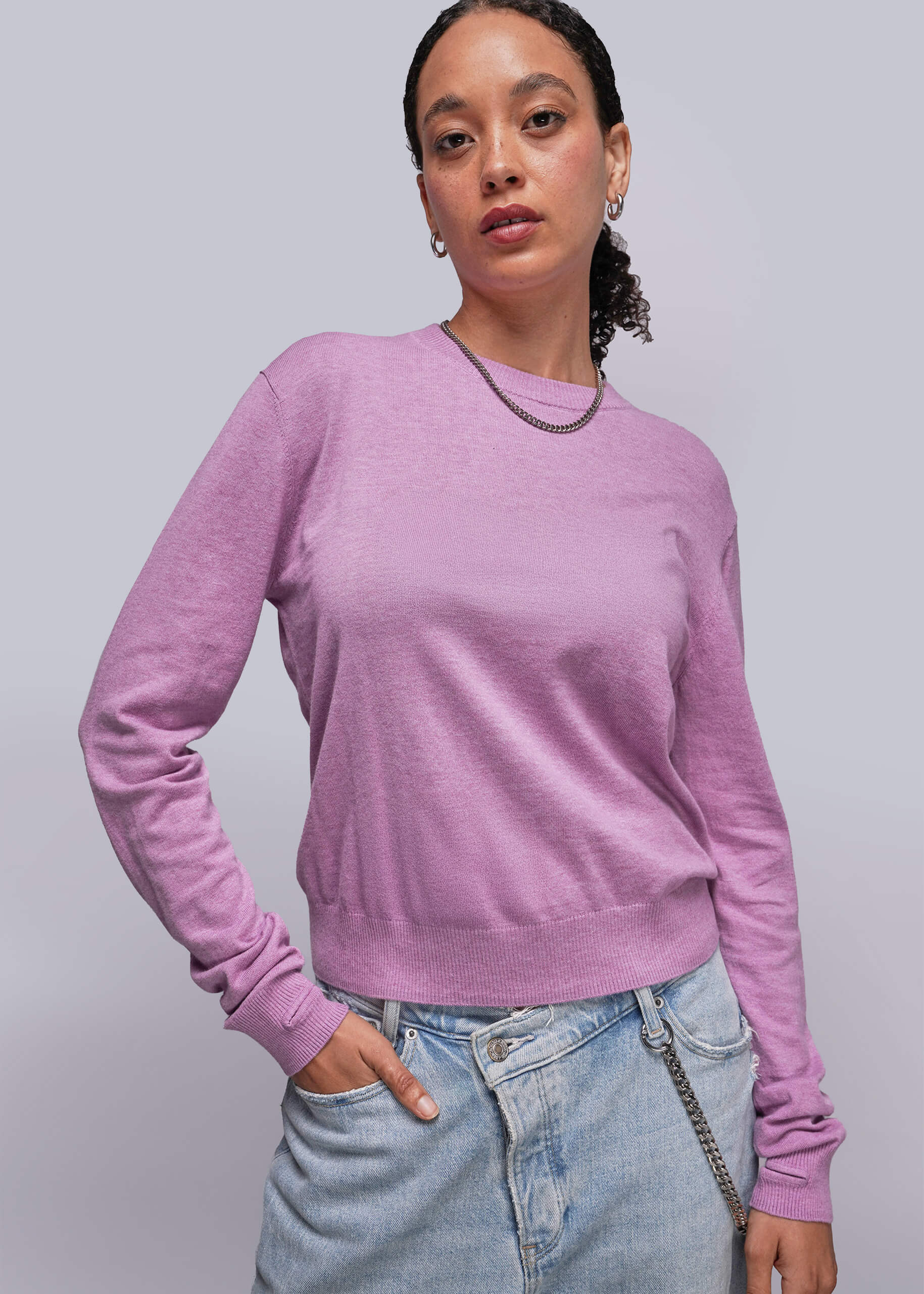 Person wearing a pink sweater and light blue jeans against a plain background