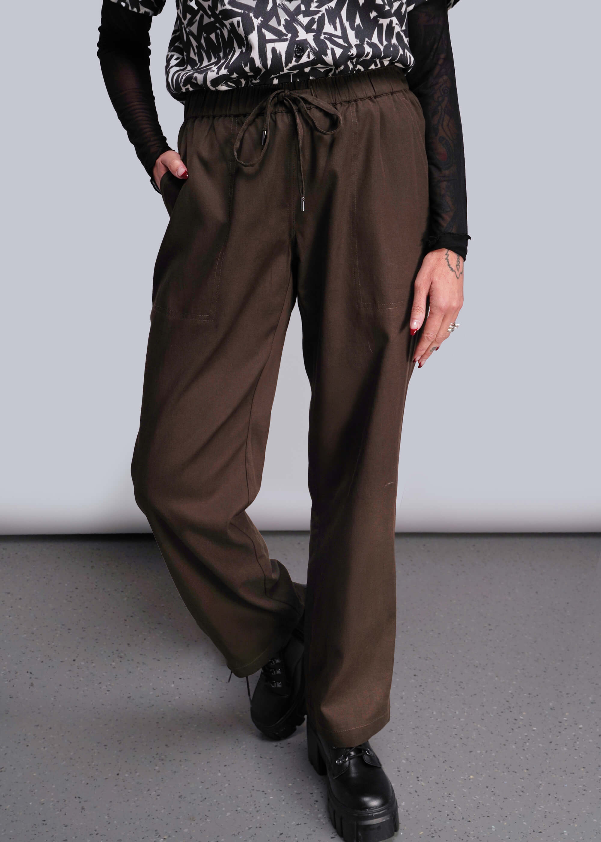 Person wearing brown pants and black shoes on a plain background
