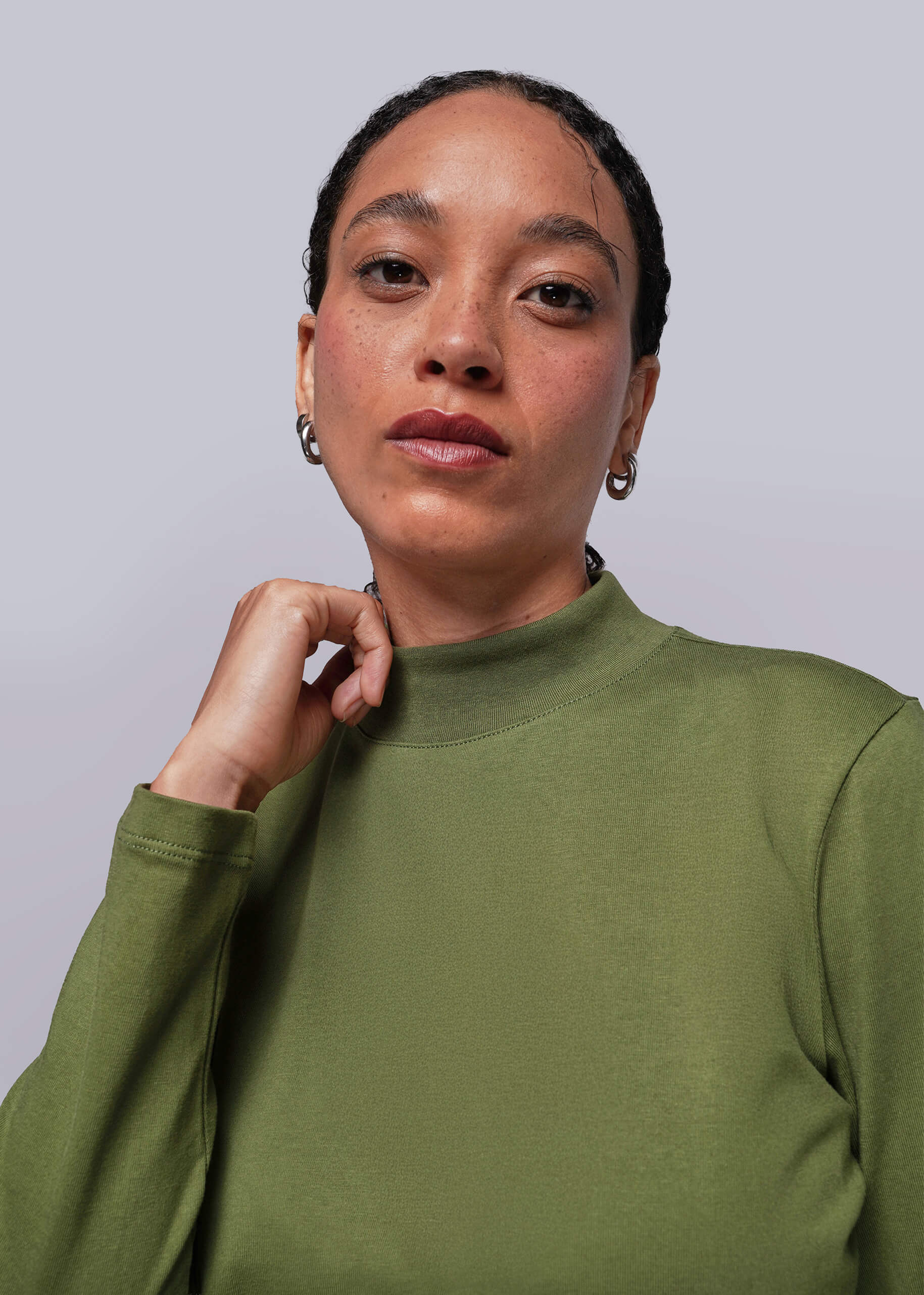 Person wearing a green long sleeve shirt holding mock neck collar against a plain background