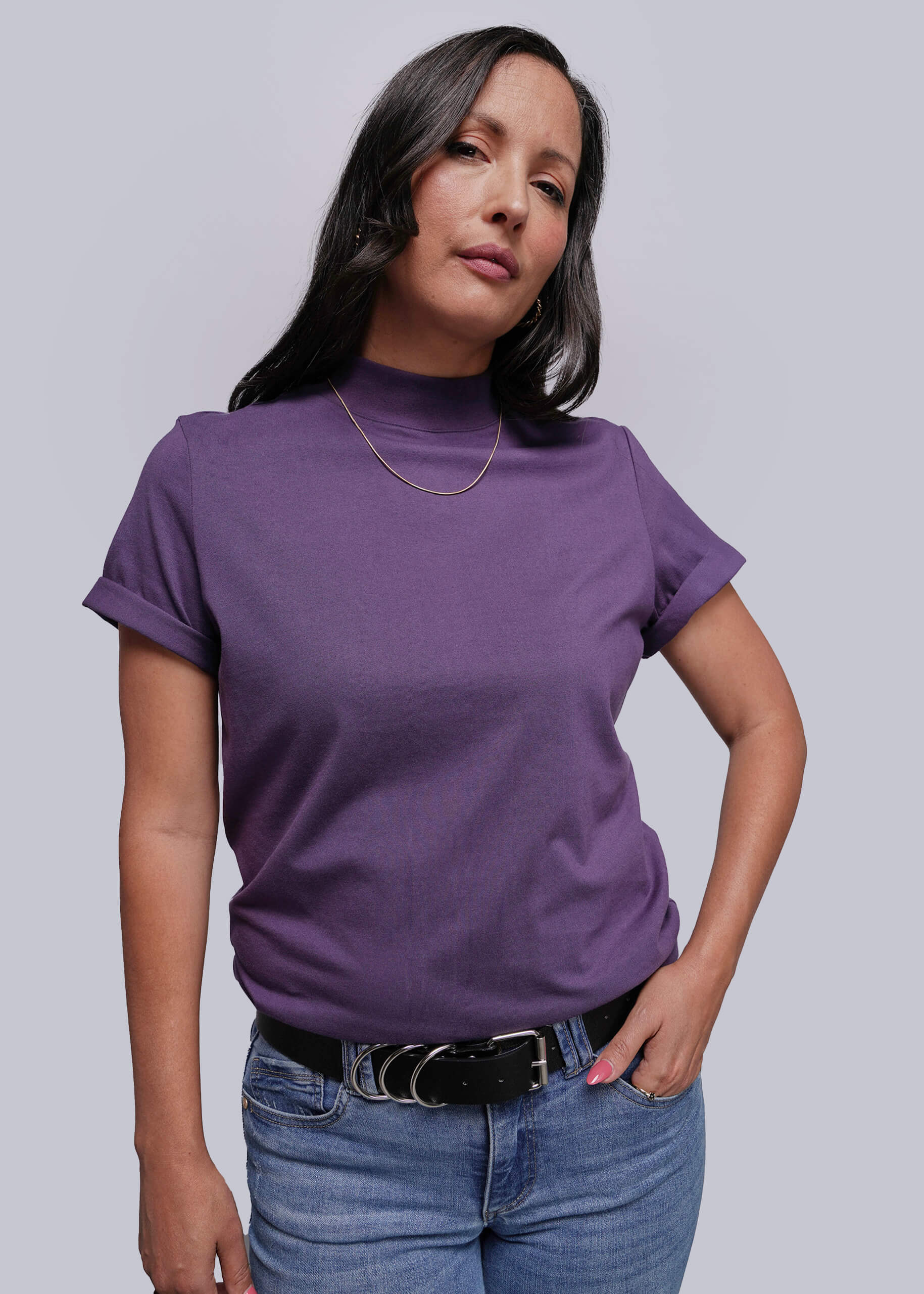 Woman wearing a purple turtleneck shirt and blue jeans against a plain background