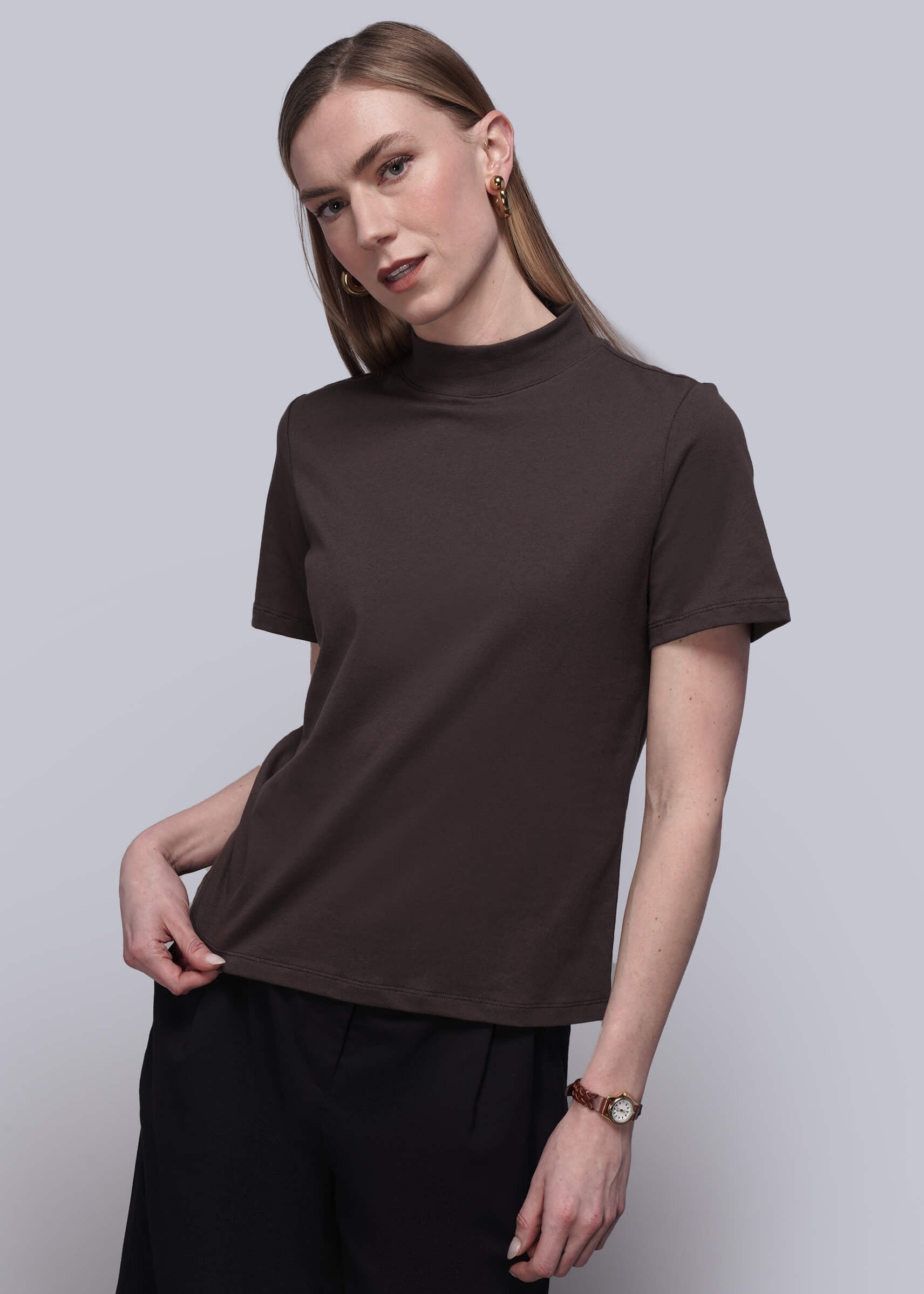 Woman wearing a brown t-shirt and black pants against a light gray background