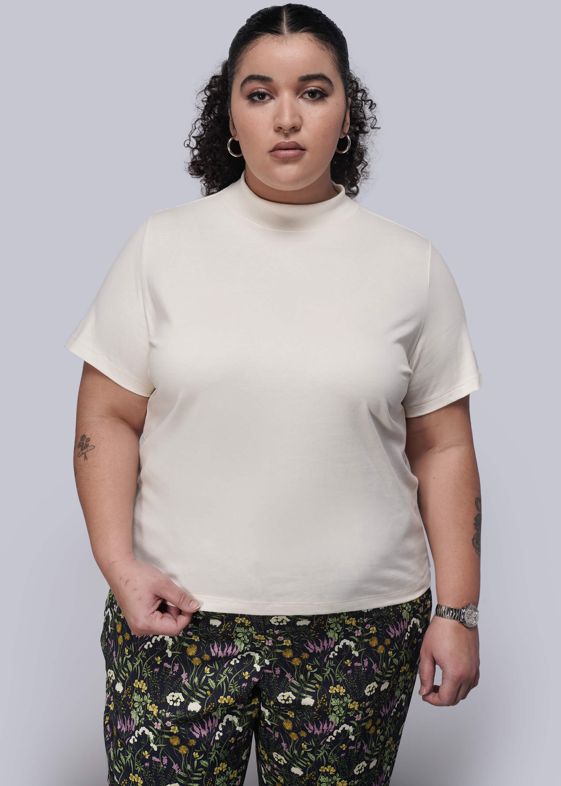 1X=Person wearing a beige t-shirt and floral pants on a plain background